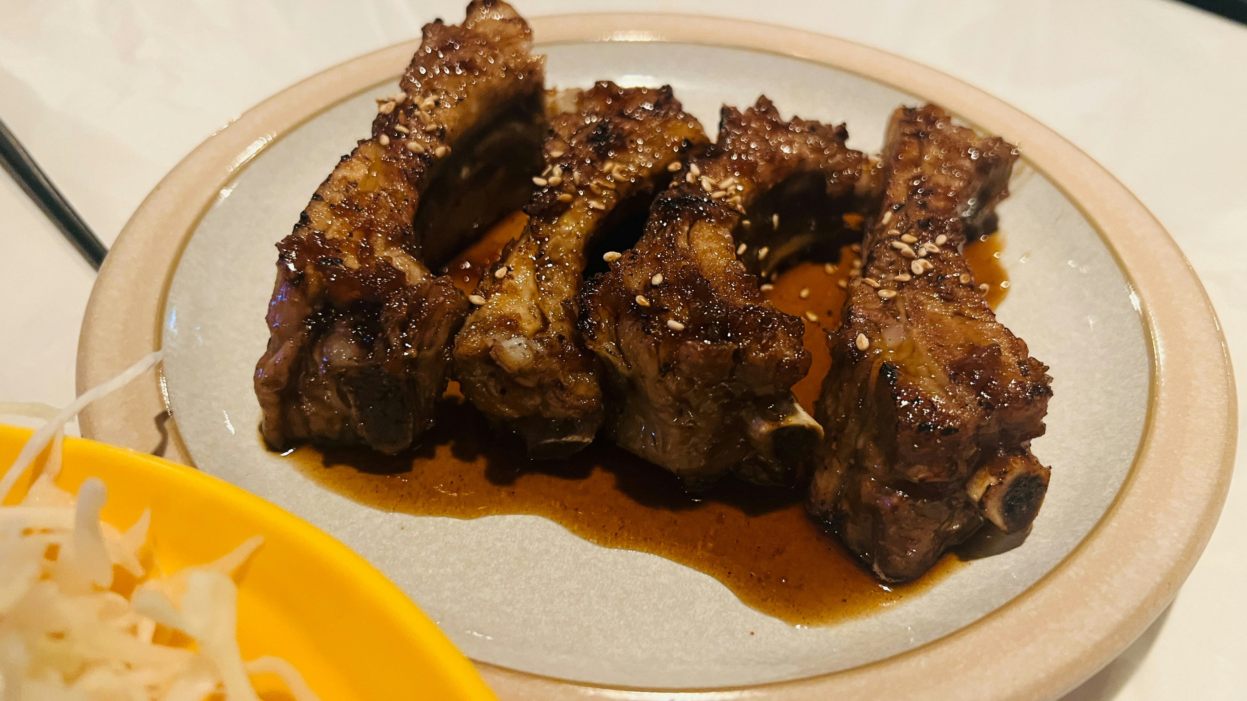Four glazed pork ribs sprinkled with sesame seeds on a ceramic plate