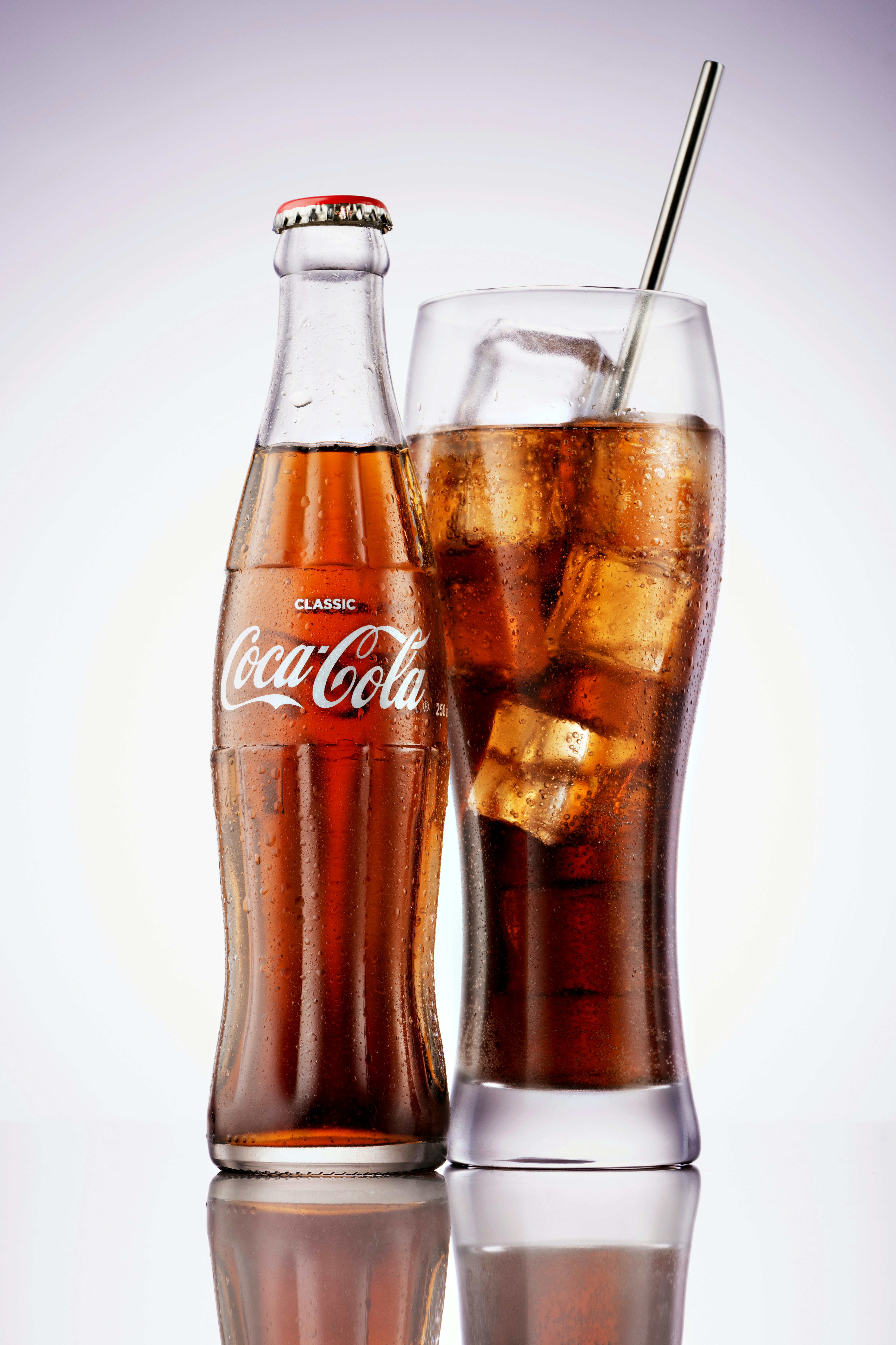 Une bouteille en verre et un verre de cola avec de la glace et une paille