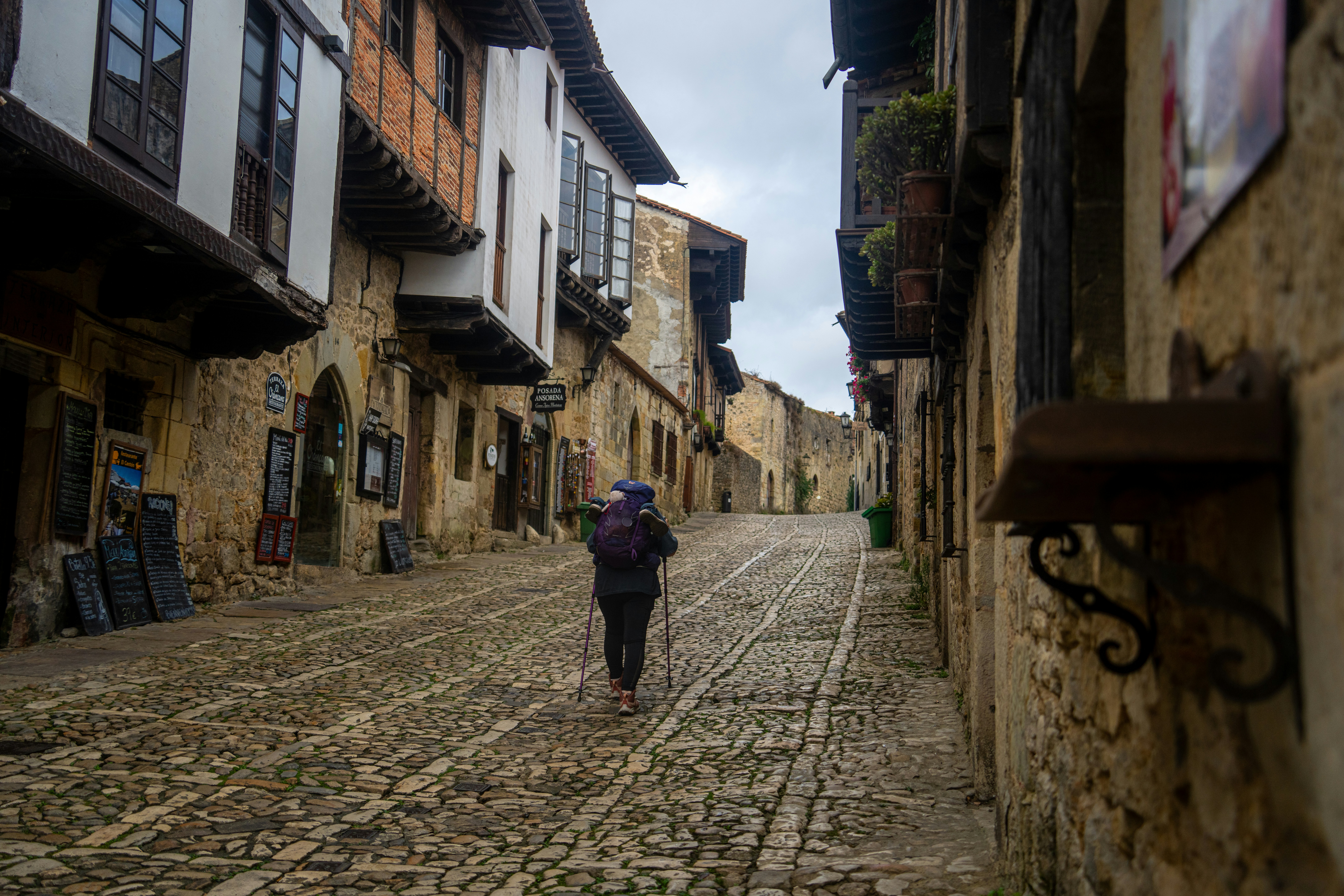 A hiker with a backpack and trekking poles walking up a cobblestone street