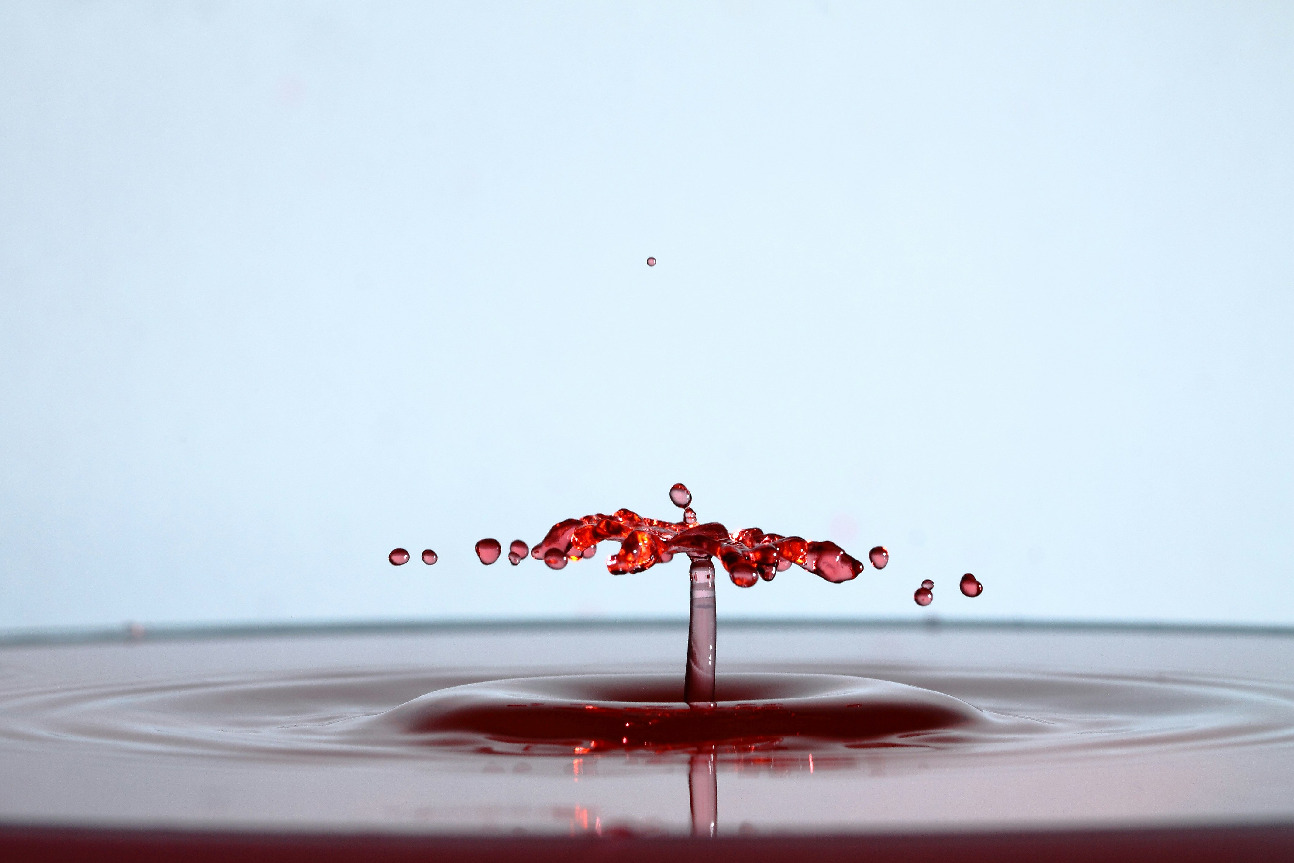 A red liquid drop creating a splash and crown shape on a surface