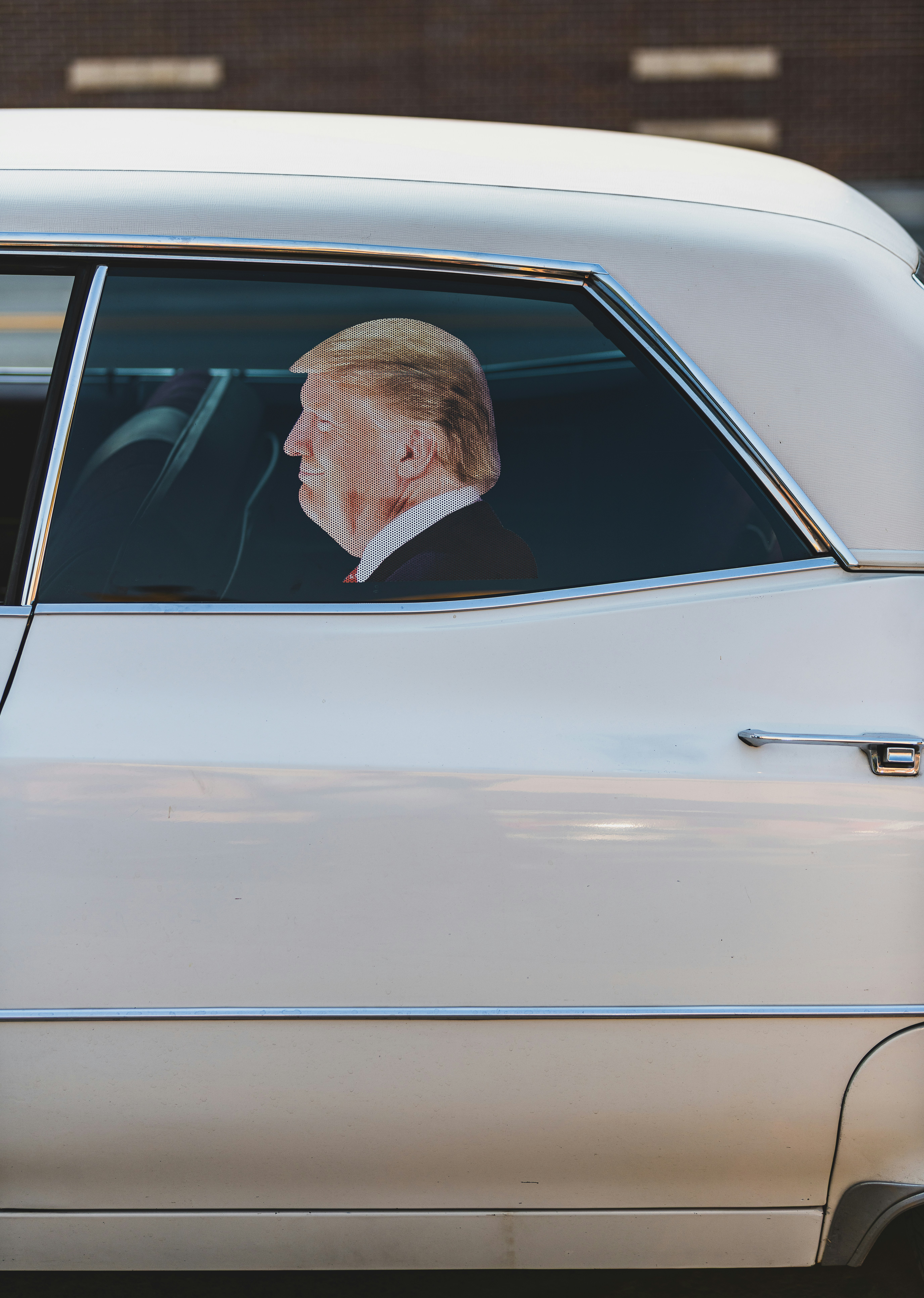 A profile portrait of Donald Trump on a perforated window decal on a white car