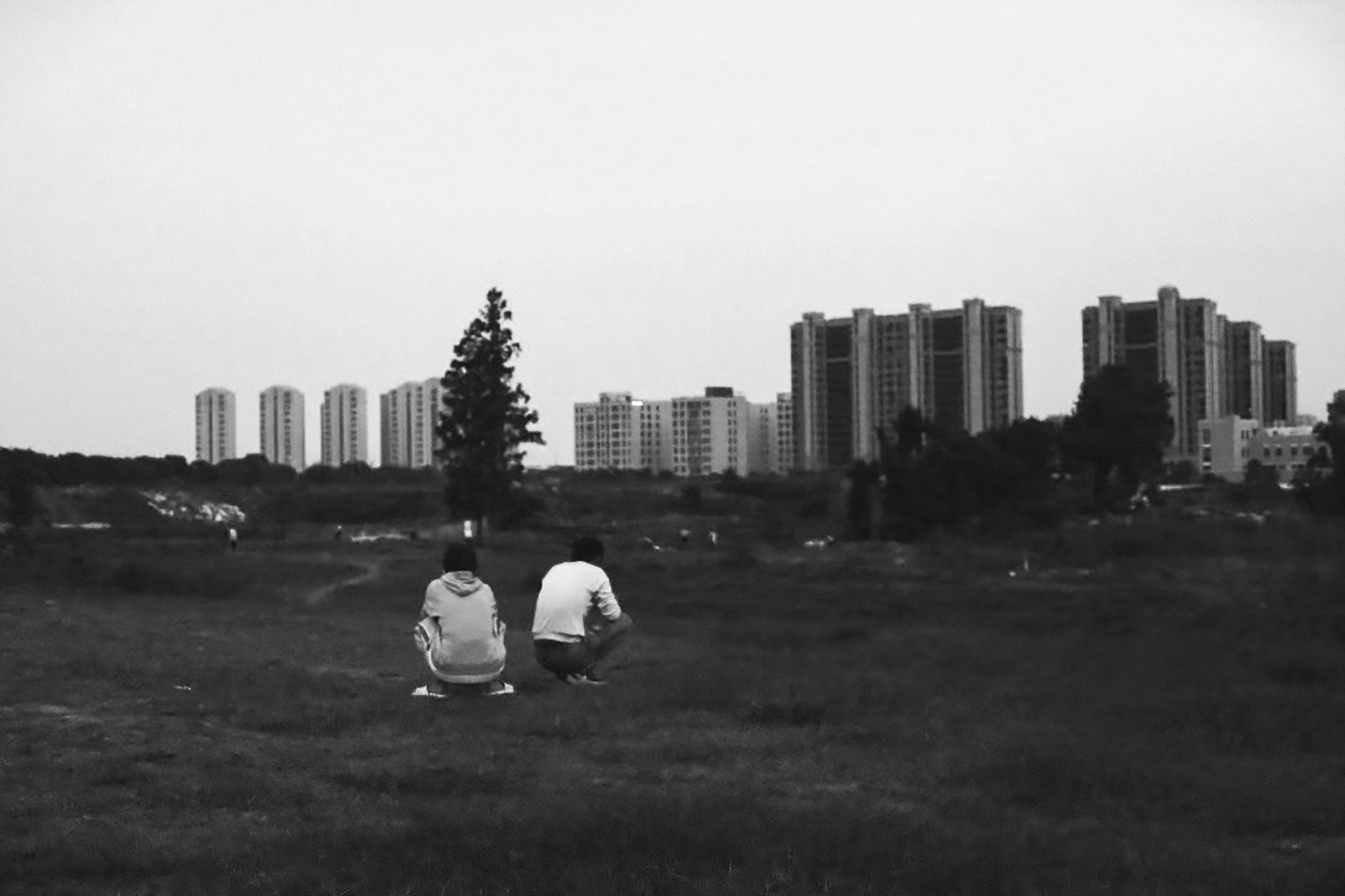 Two people crouching in a grassy field before a distant city skyline