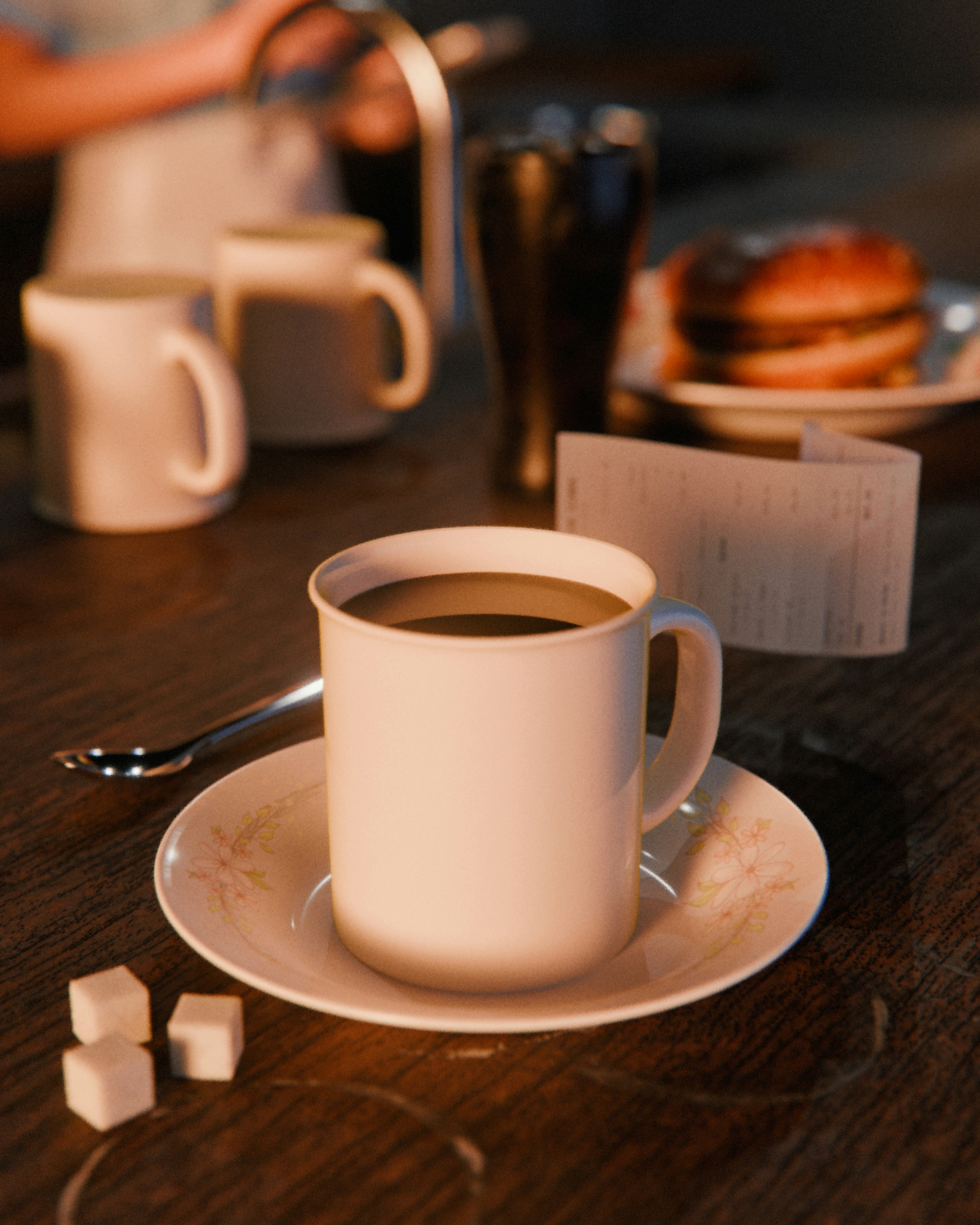 A white coffee mug on a floral saucer with sugar cubes on a table