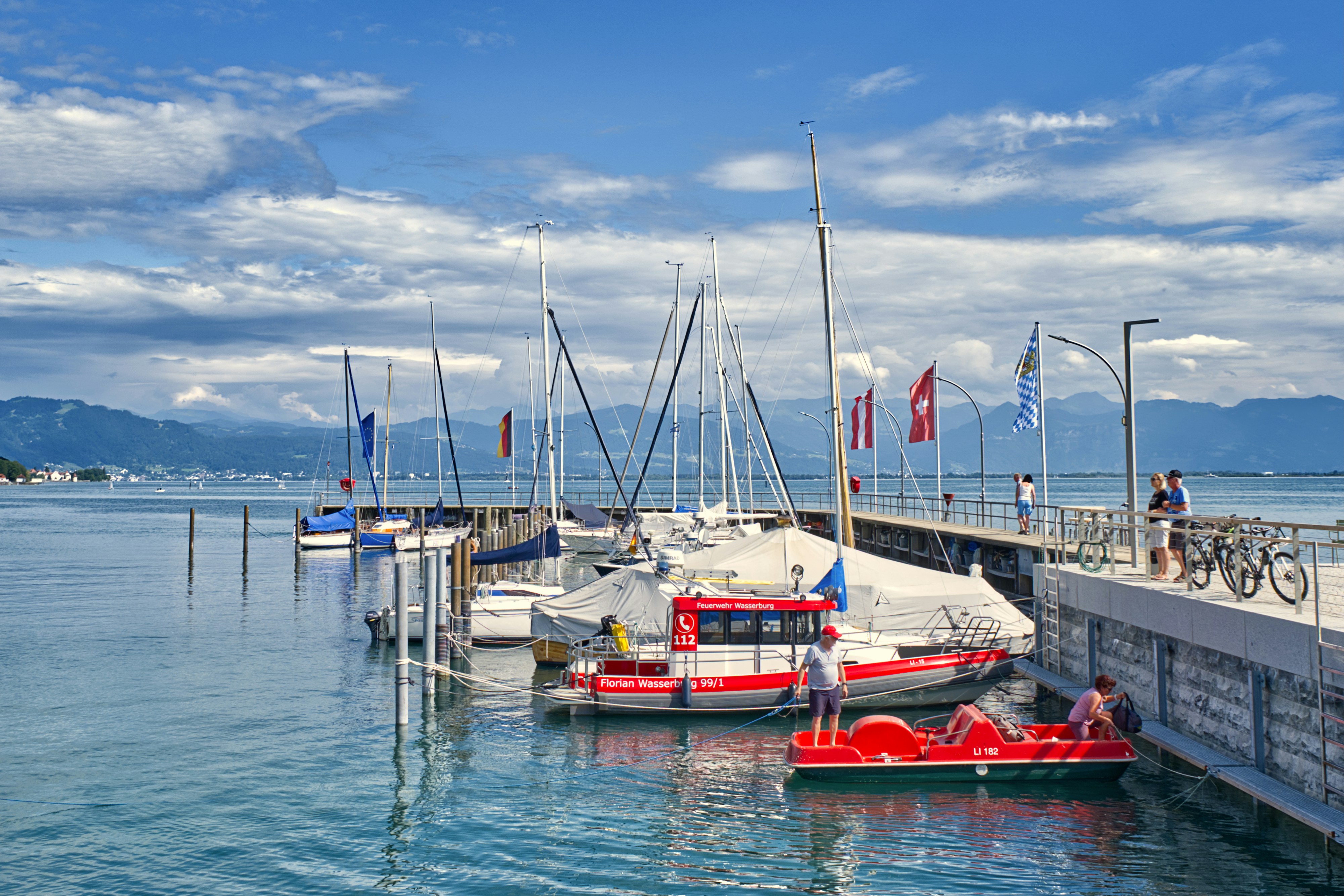 Sailboats and a red rescue boat moored at a pier on Lake Constance