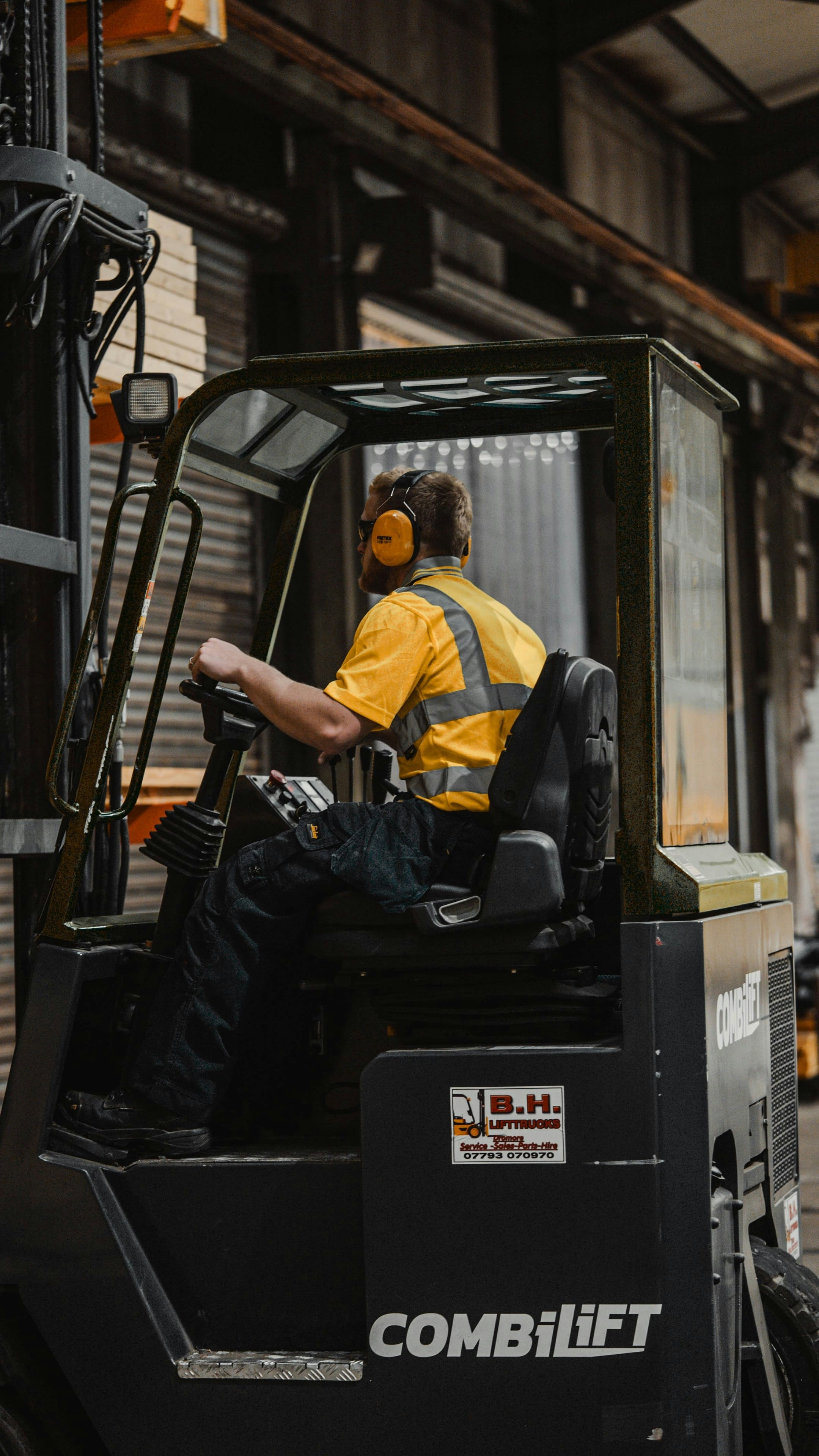 A person in a yellow high-visibility shirt operating a Combilift forklift in a warehouse