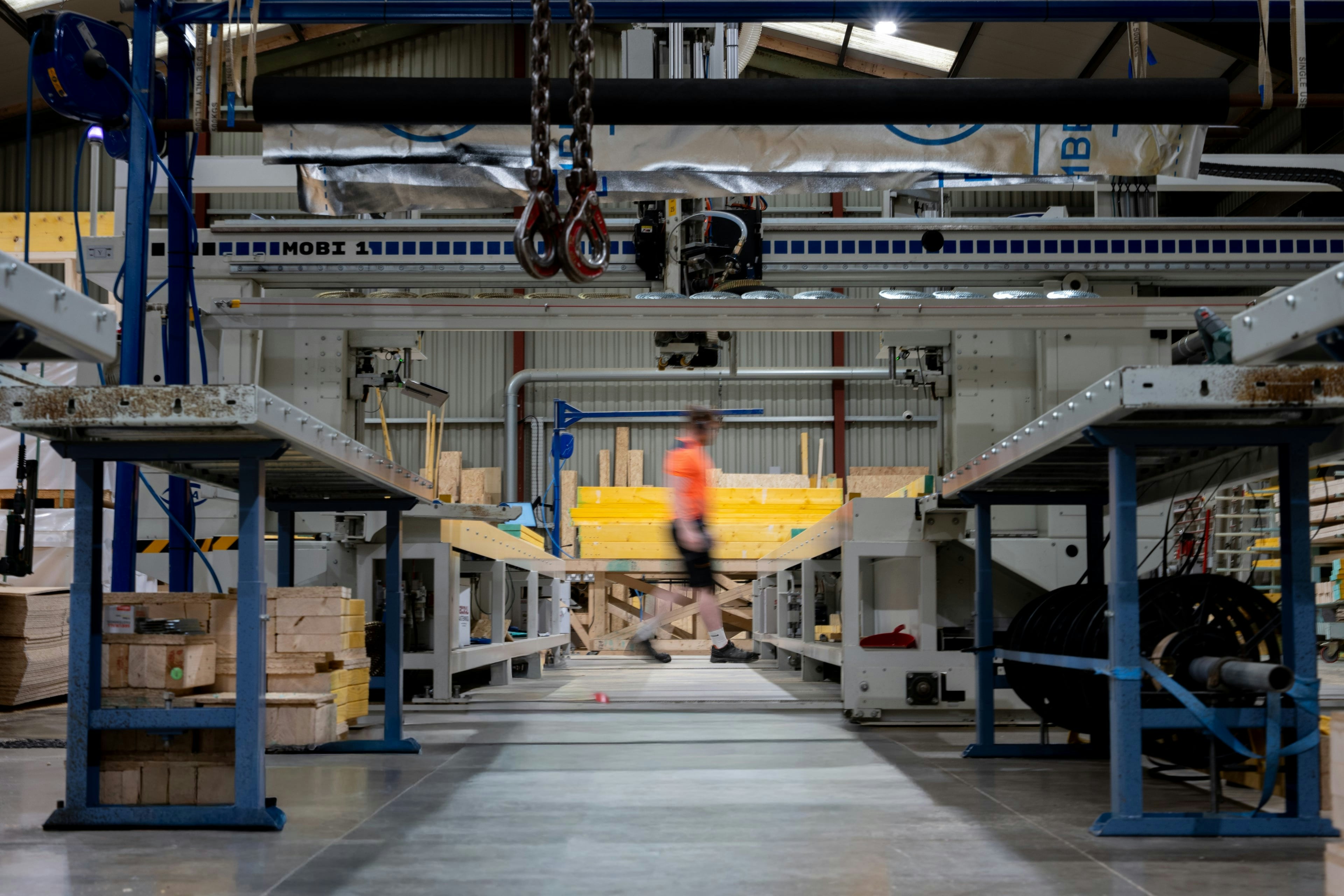 A worker moves along an industrial workshop aisle, foreground shelving and machinery frame the scene with a shallow depth of field highlighting the central walkway.