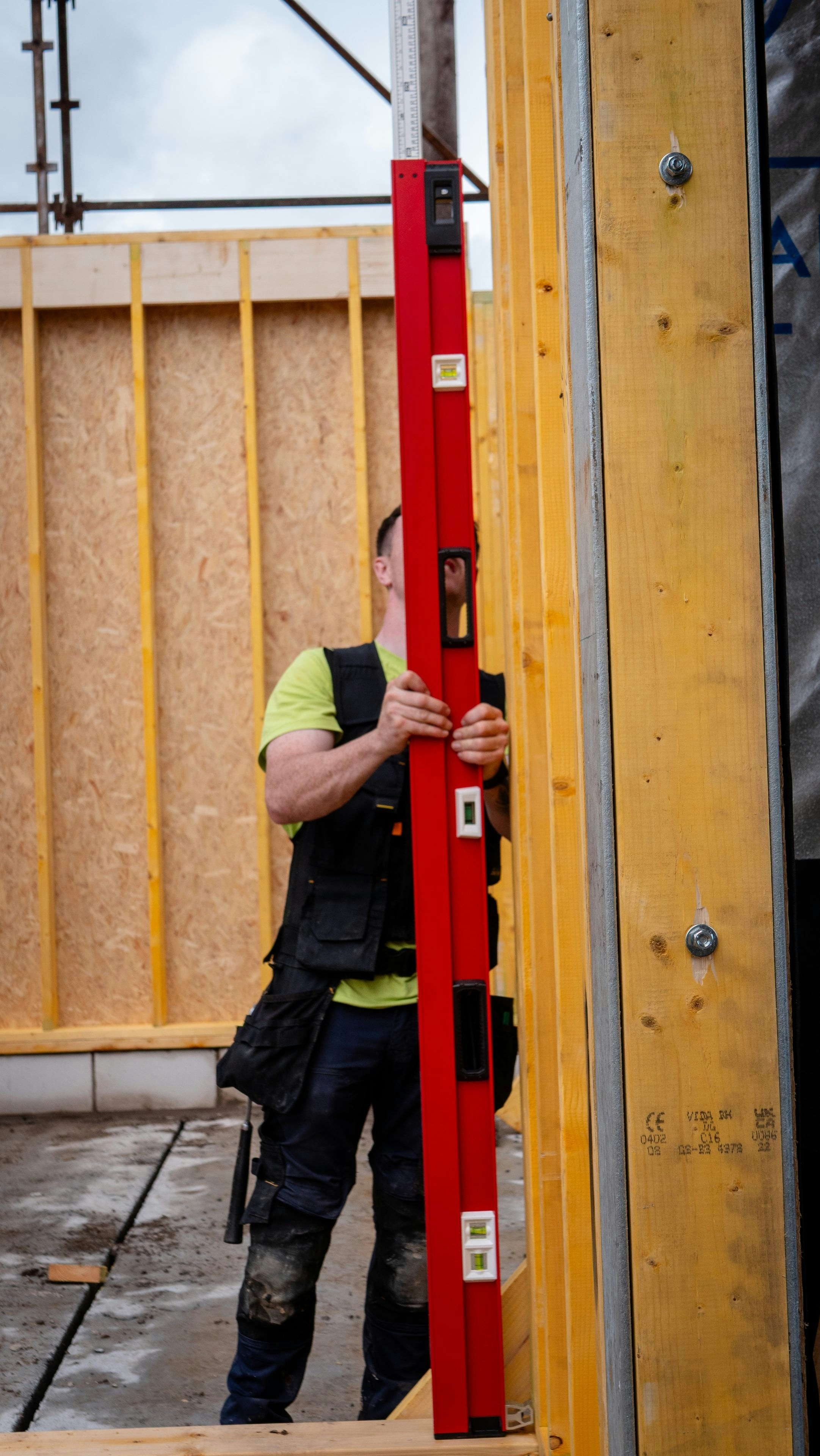 En tømrer holder et langt vater mot et veggelement av stendere og plater.