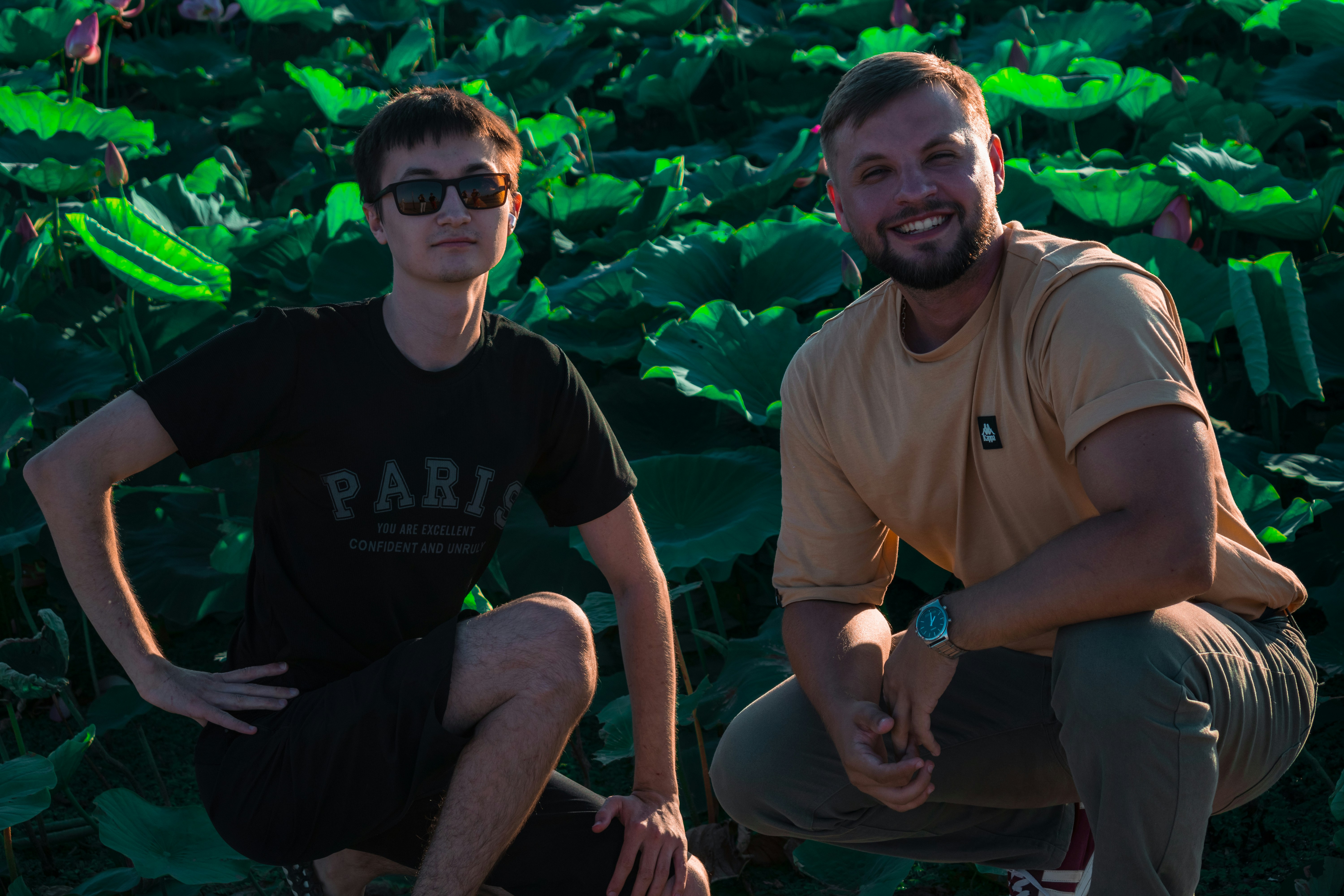 Two men crouching in a field of large green lotus leaves