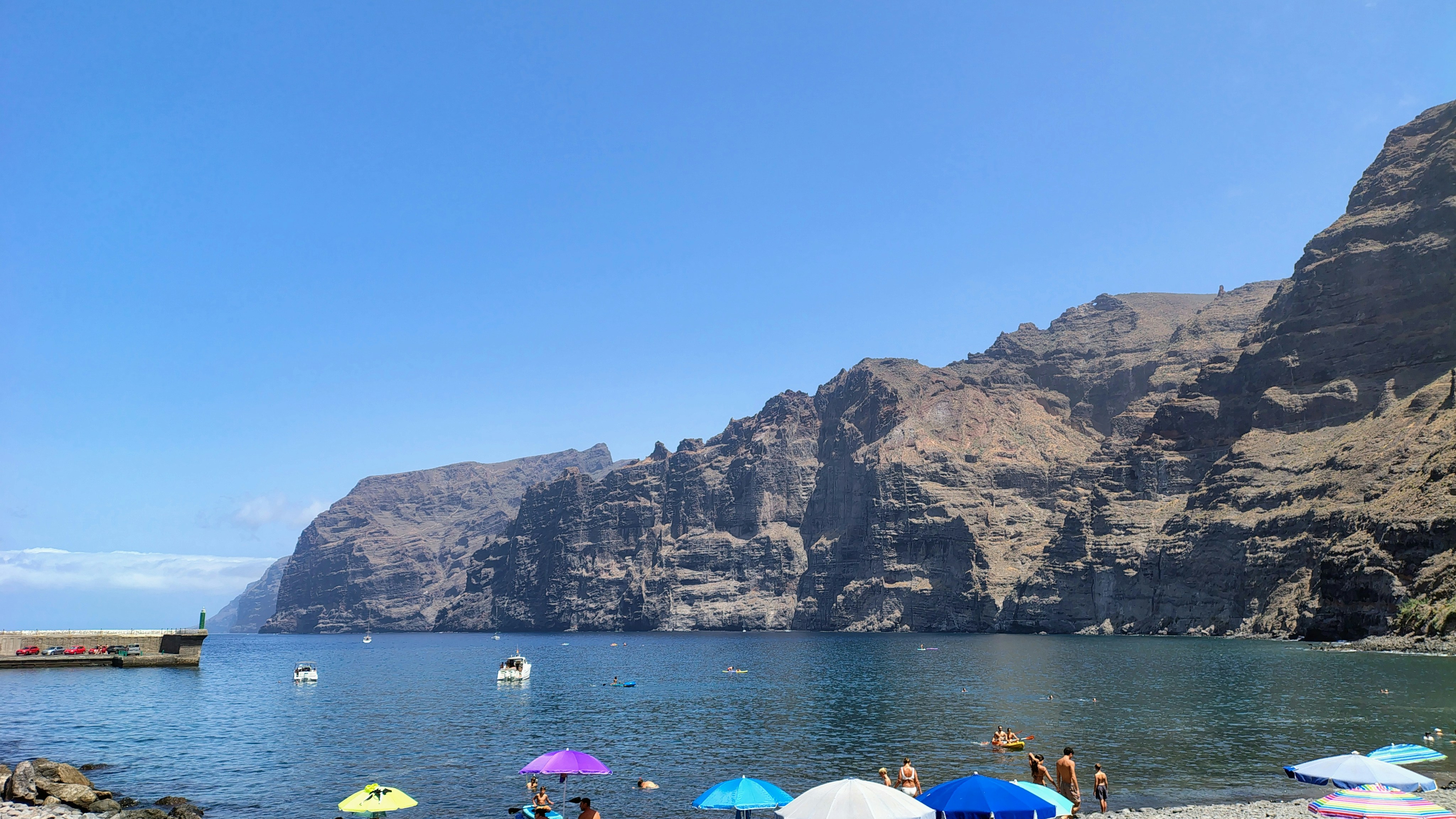 People on a beach with colorful umbrellas below towering rocky cliffs by the sea