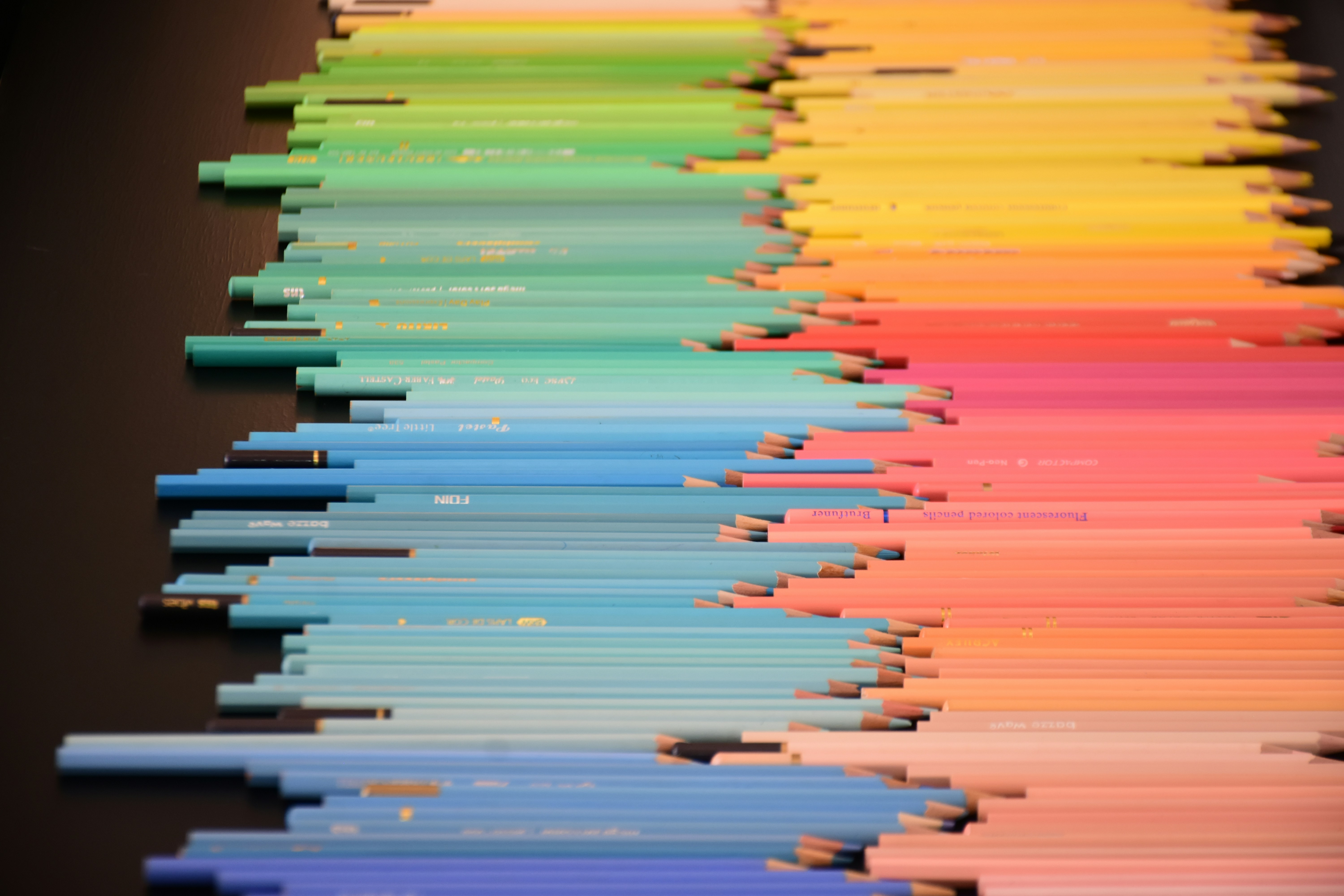 A gradient of colored pencils arranged in rows on a dark surface