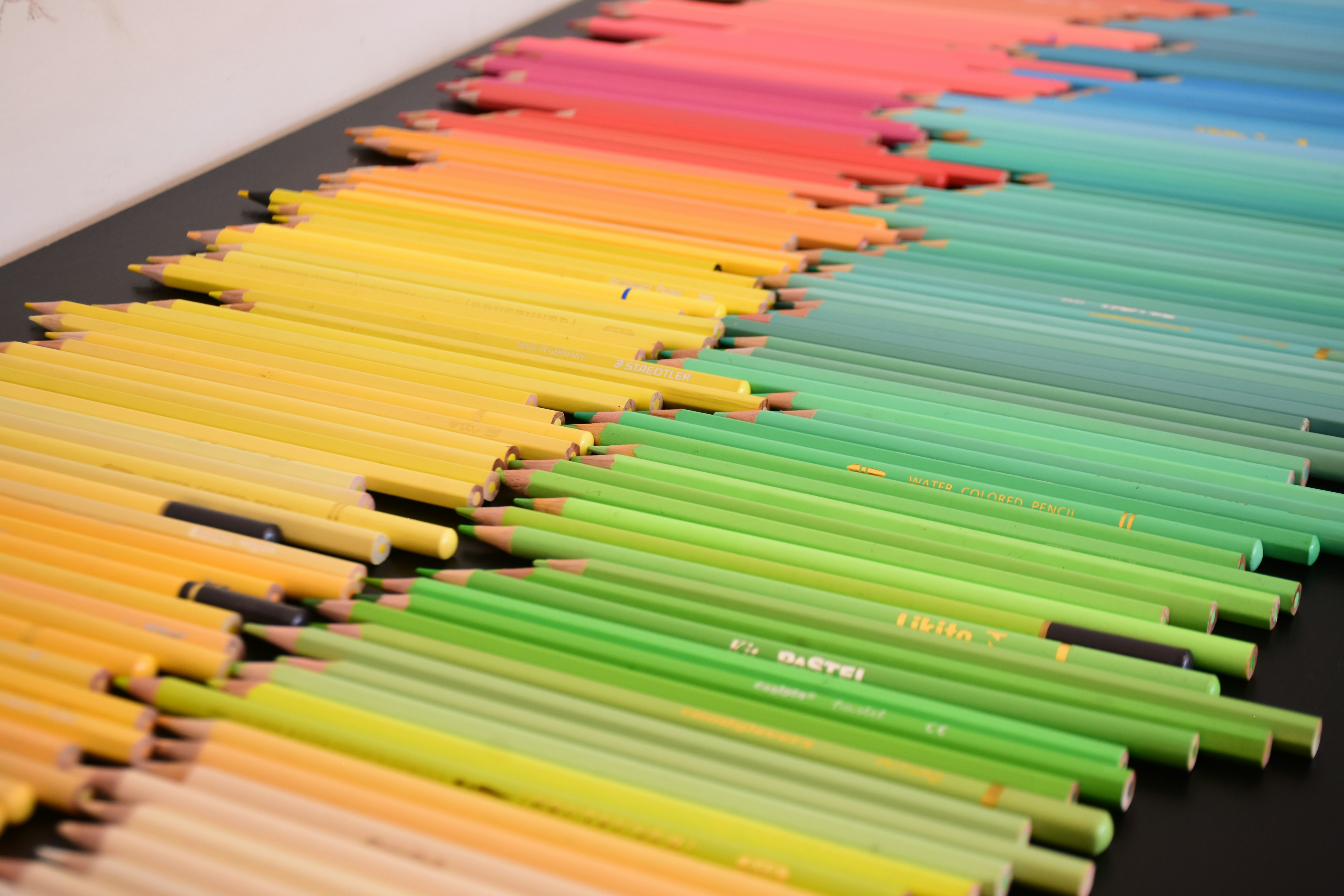 A collection of colored pencils arranged in a spectrum on a black surface