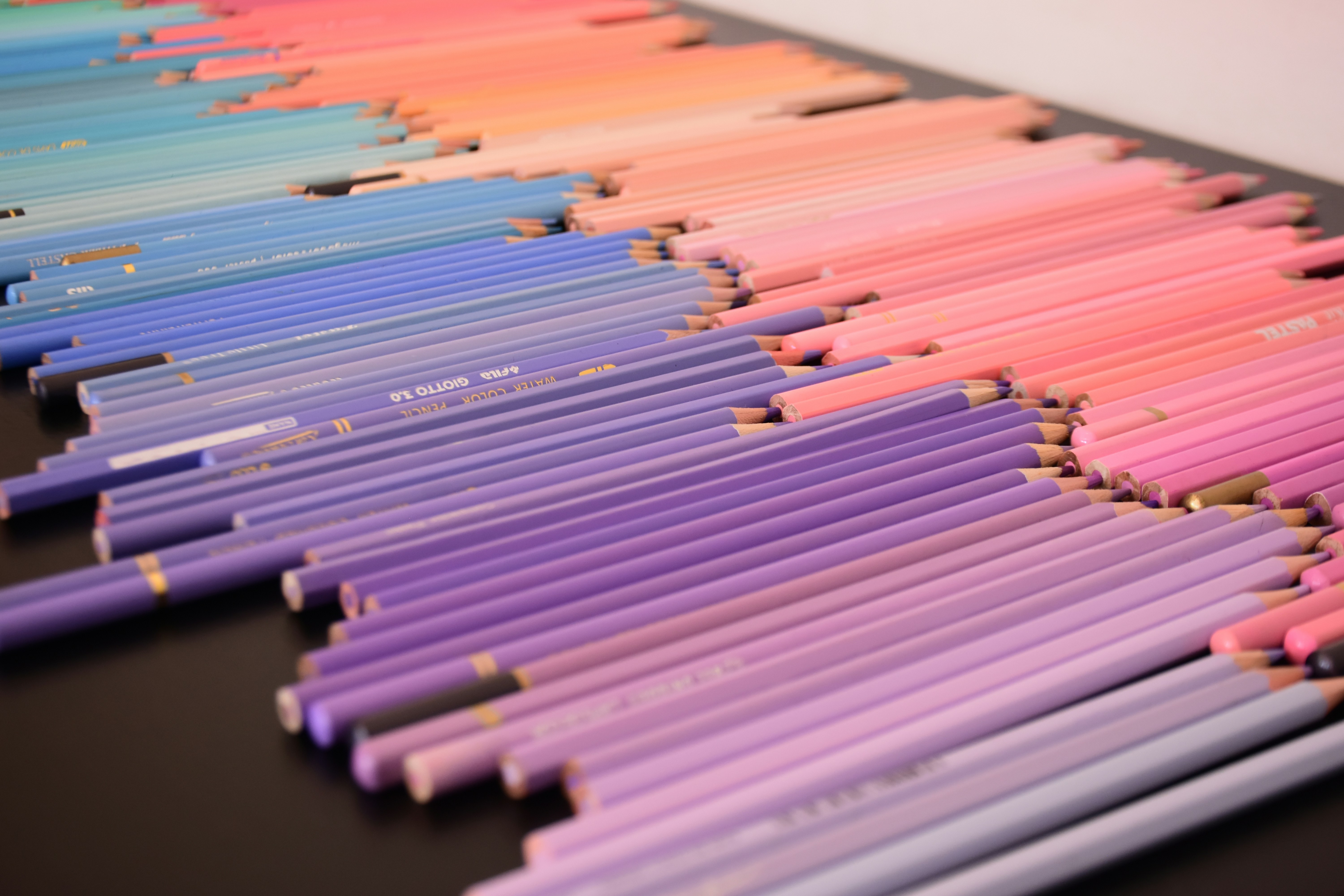 A gradient of colored pencils arranged in rows on a dark surface
