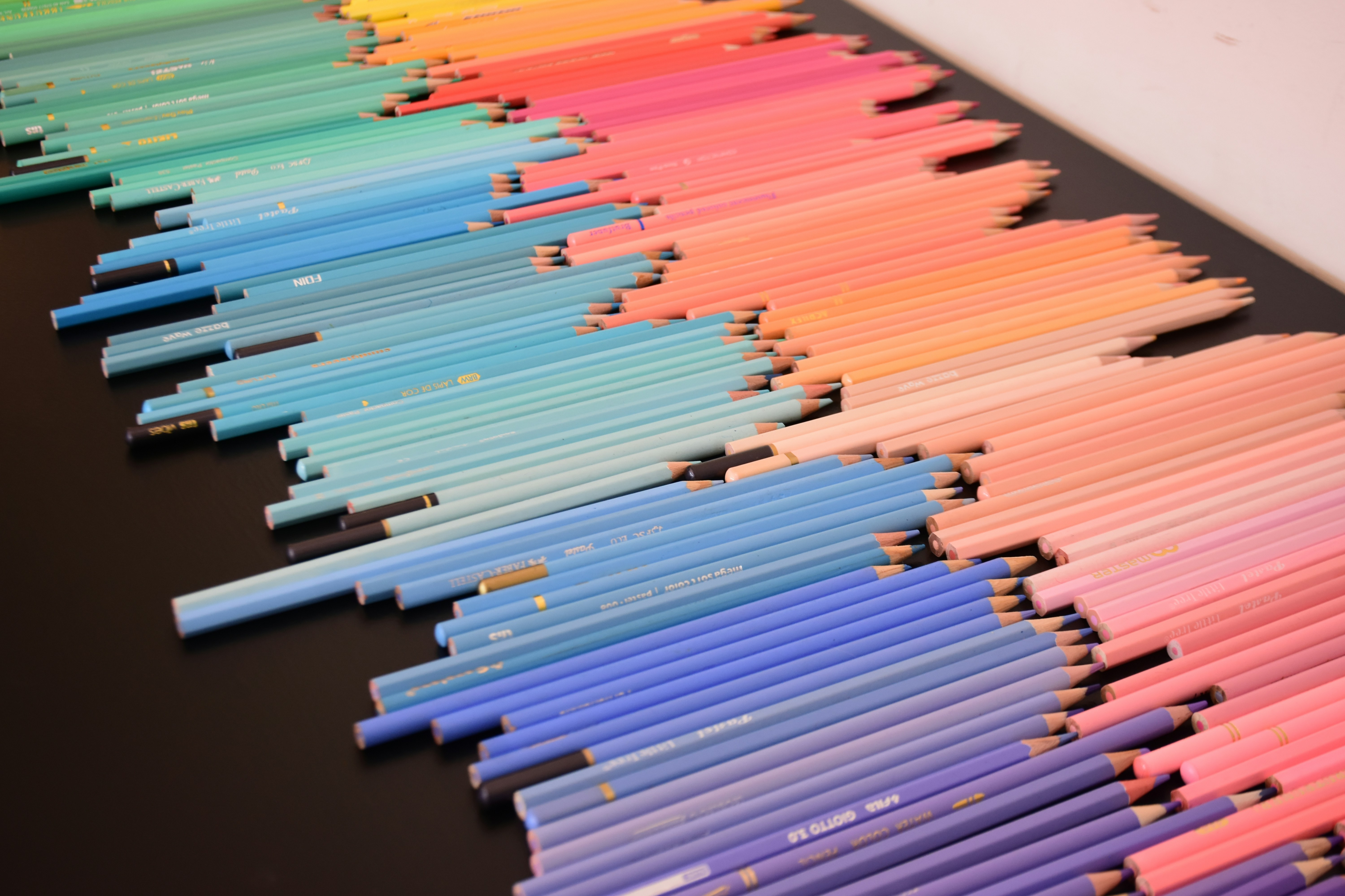 Many colored pencils arranged in a spectrum on a black surface