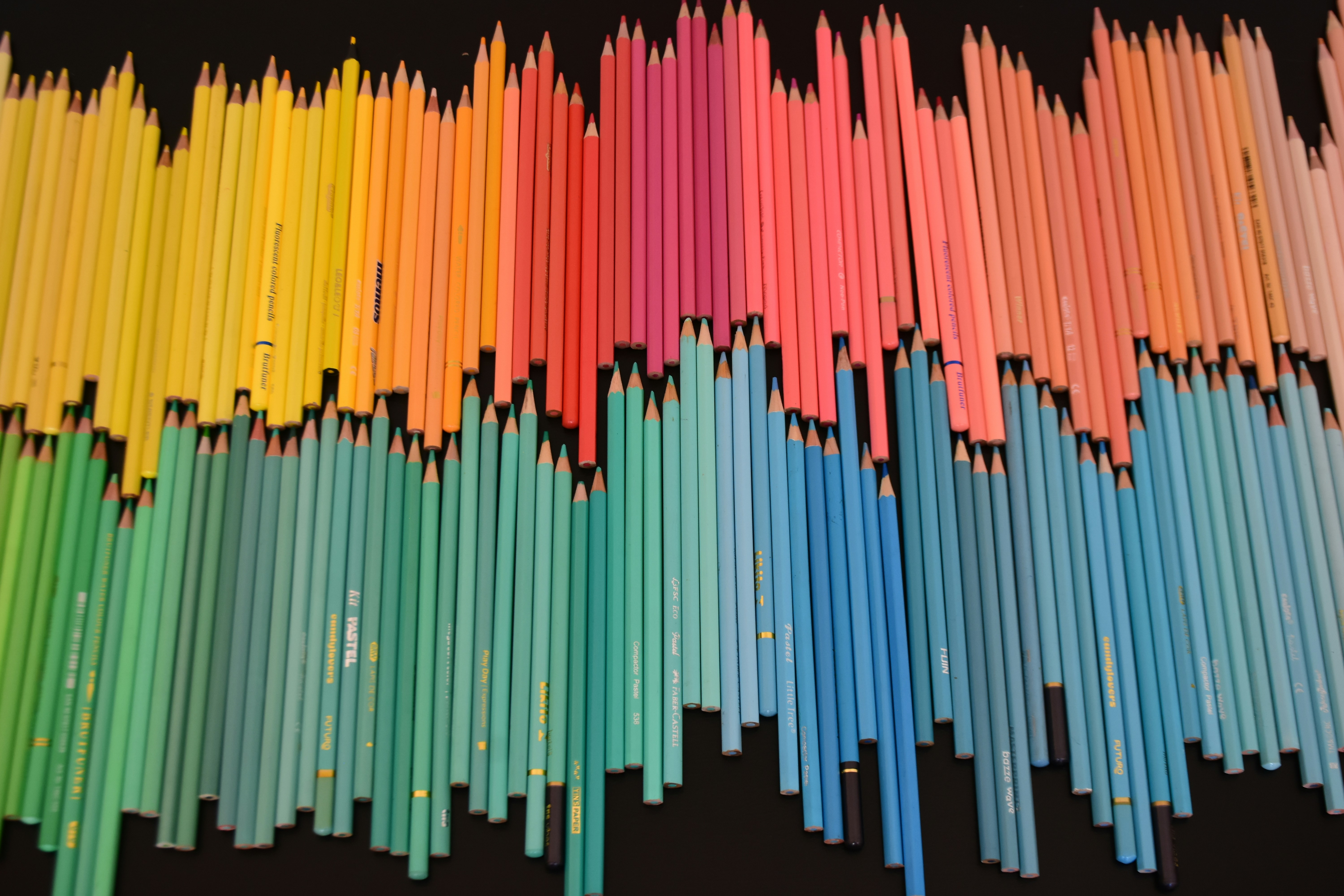 A large collection of colored pencils arranged in a spectrum on a black surface