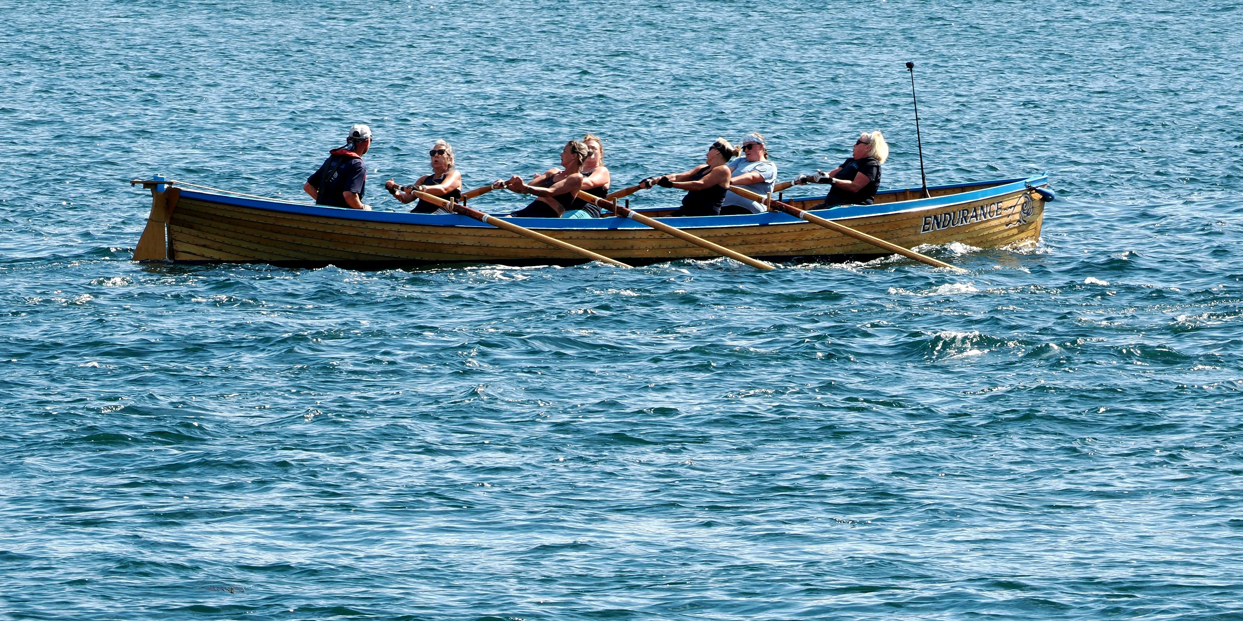 A group of people rowing a wooden boat named Endurance on blue water