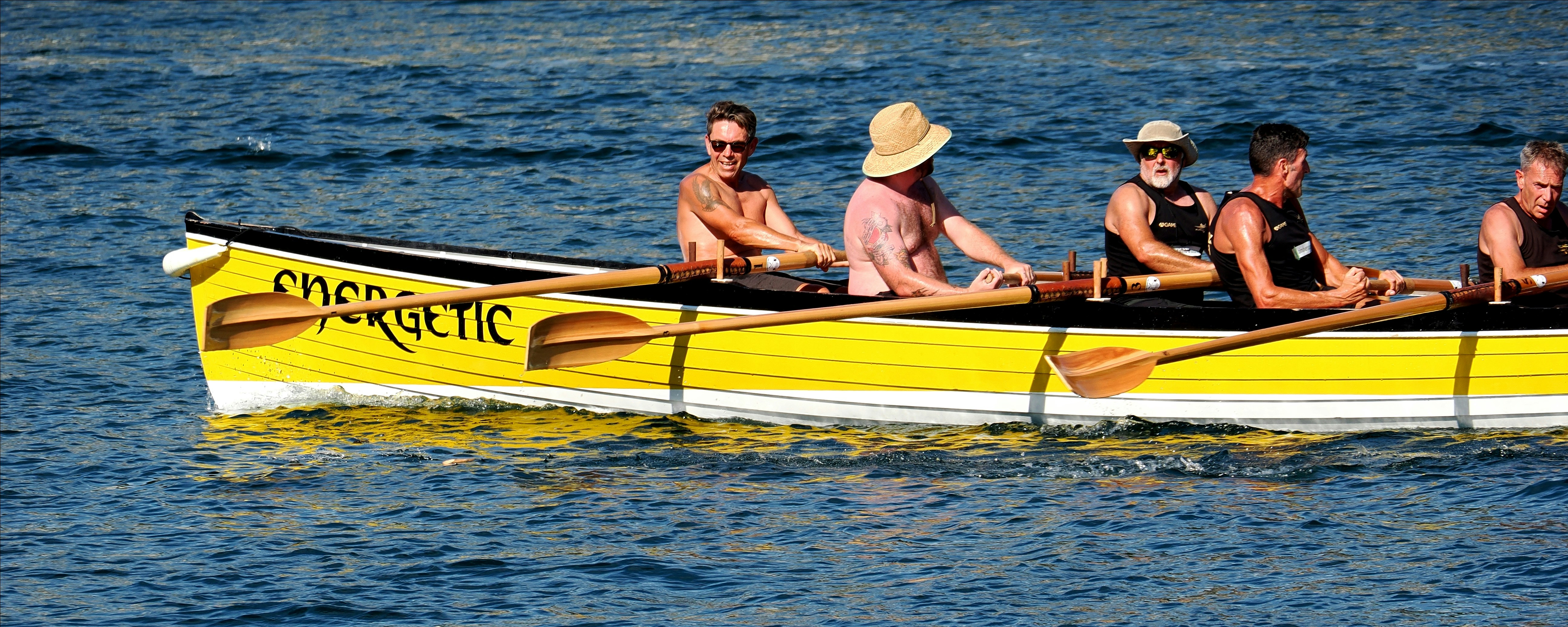 Five men rowing a yellow boat named Energetic on blue water