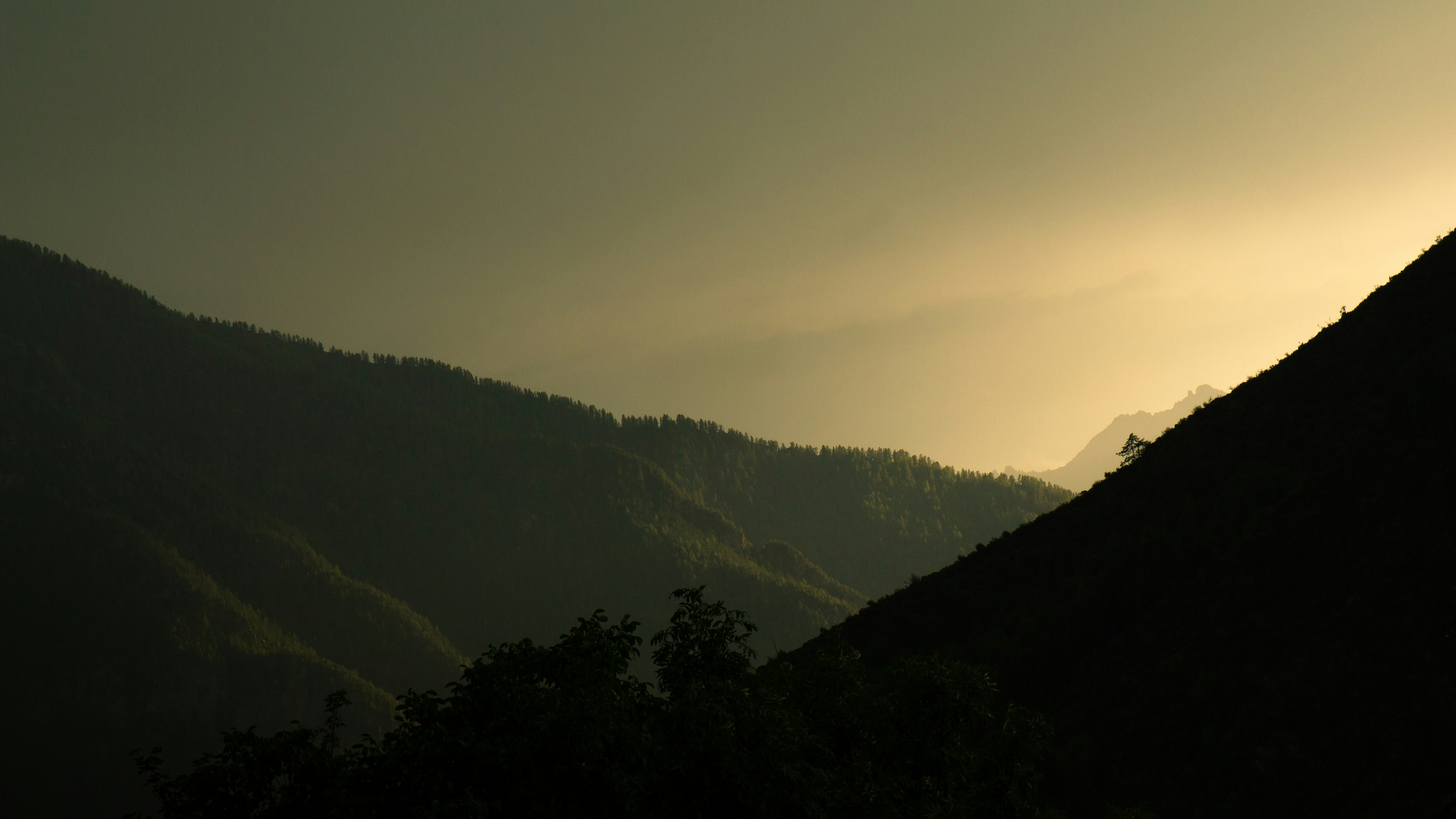 Silhouetted mountain ridges against a warm golden sky with soft light
