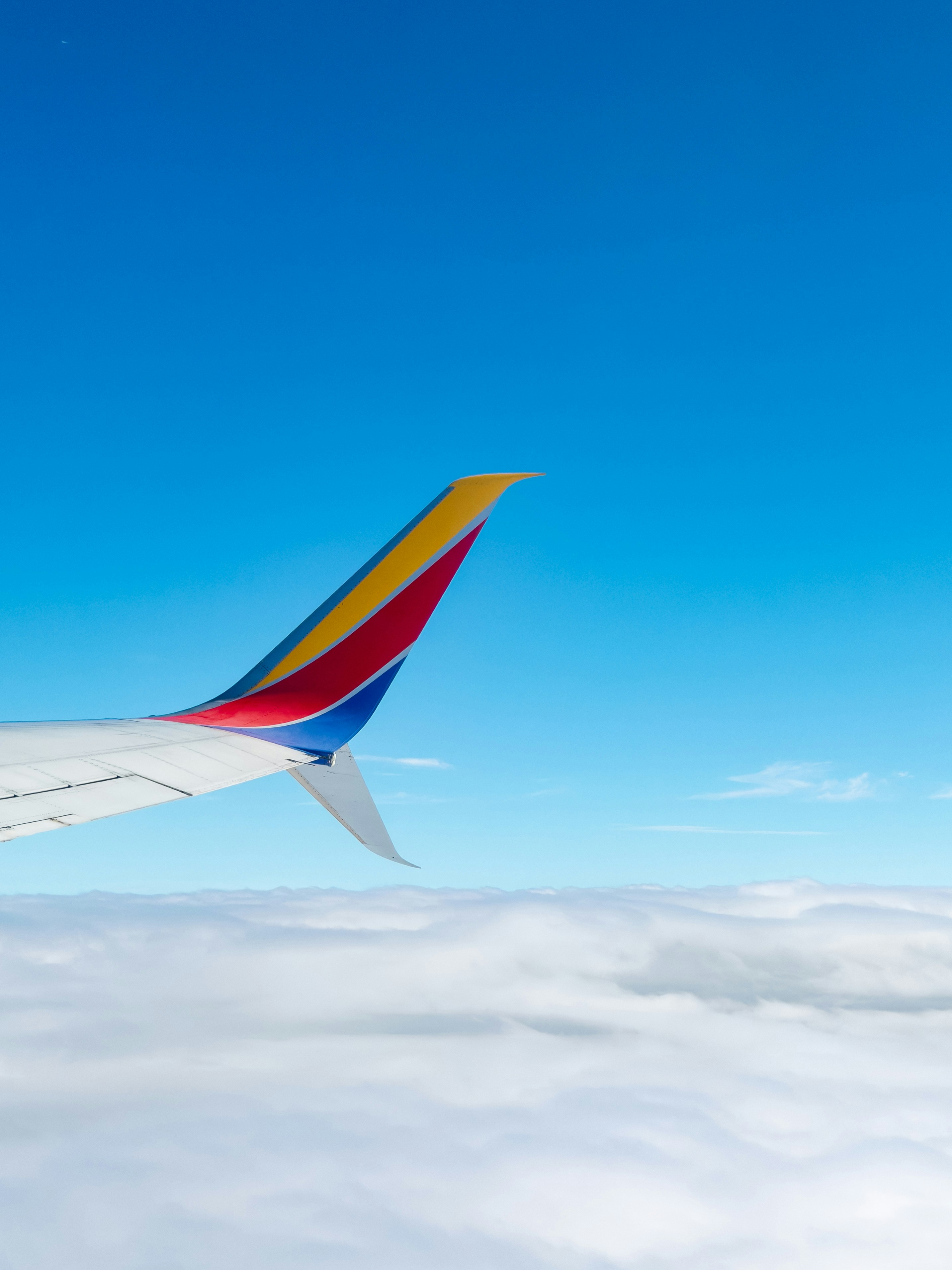 A colorful airplane winglet against a bright blue sky above a layer of clouds