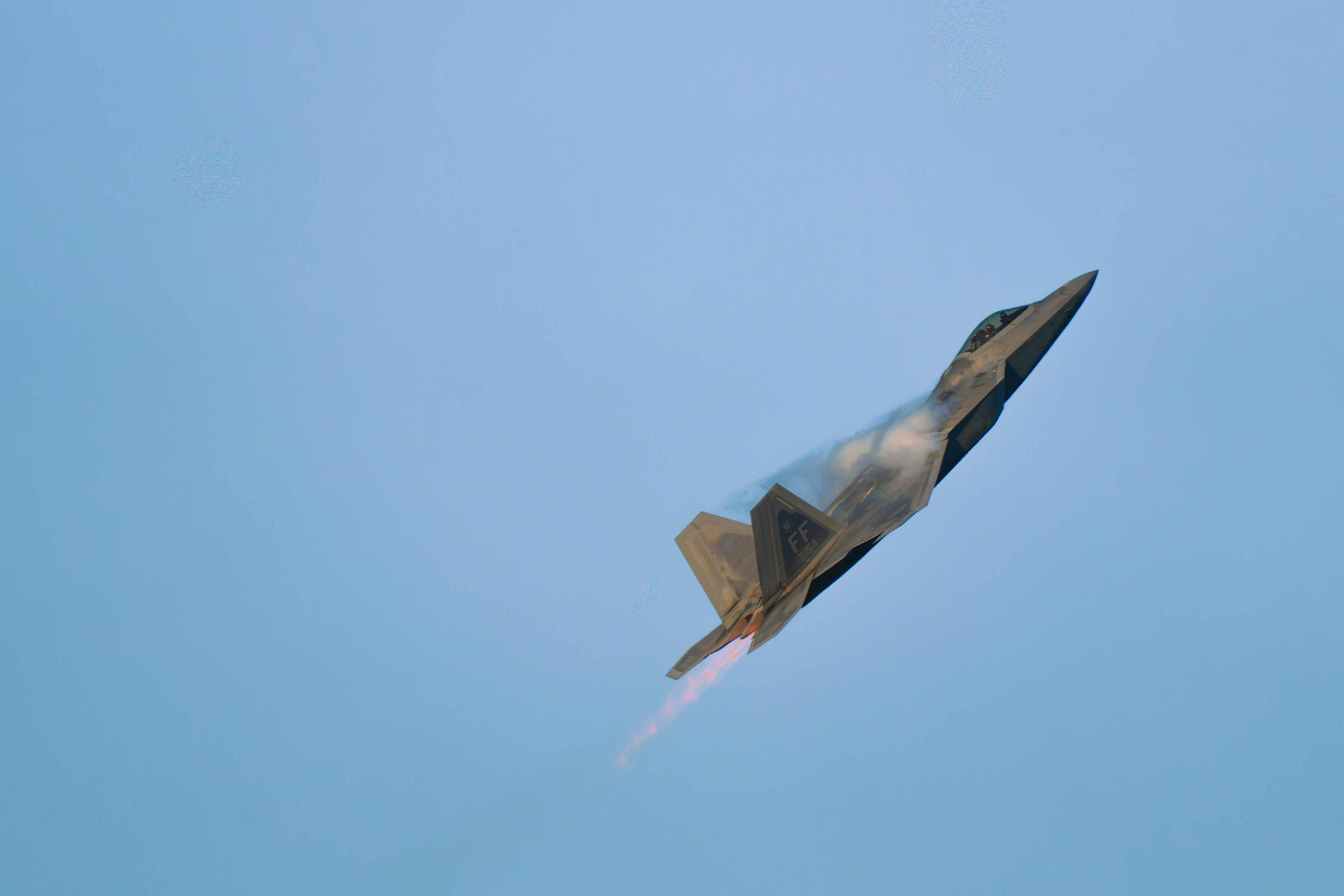 An F-22 Raptor fighter jet climbing steeply into a clear blue sky