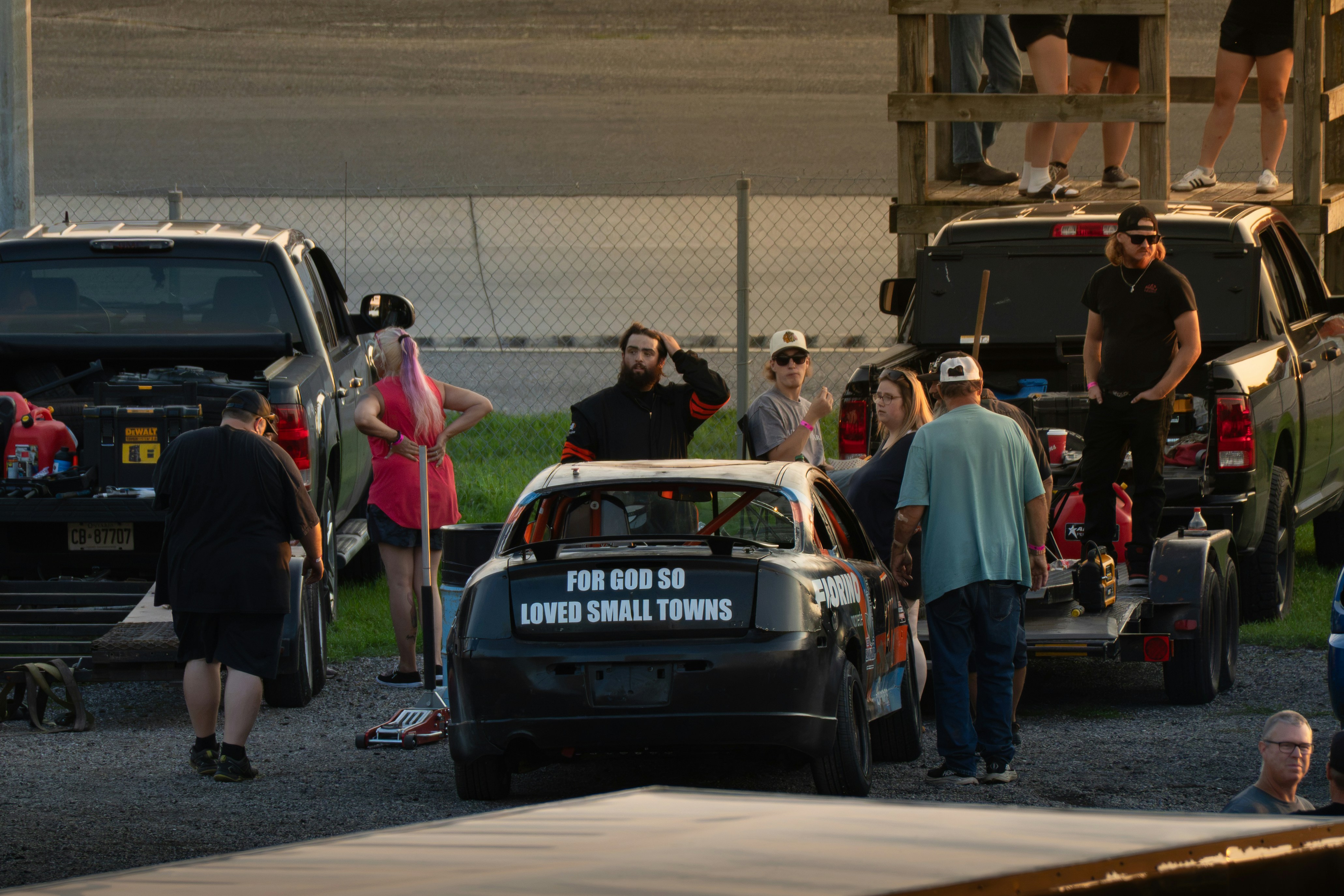 A group of people around a black stock car in a gravel lot