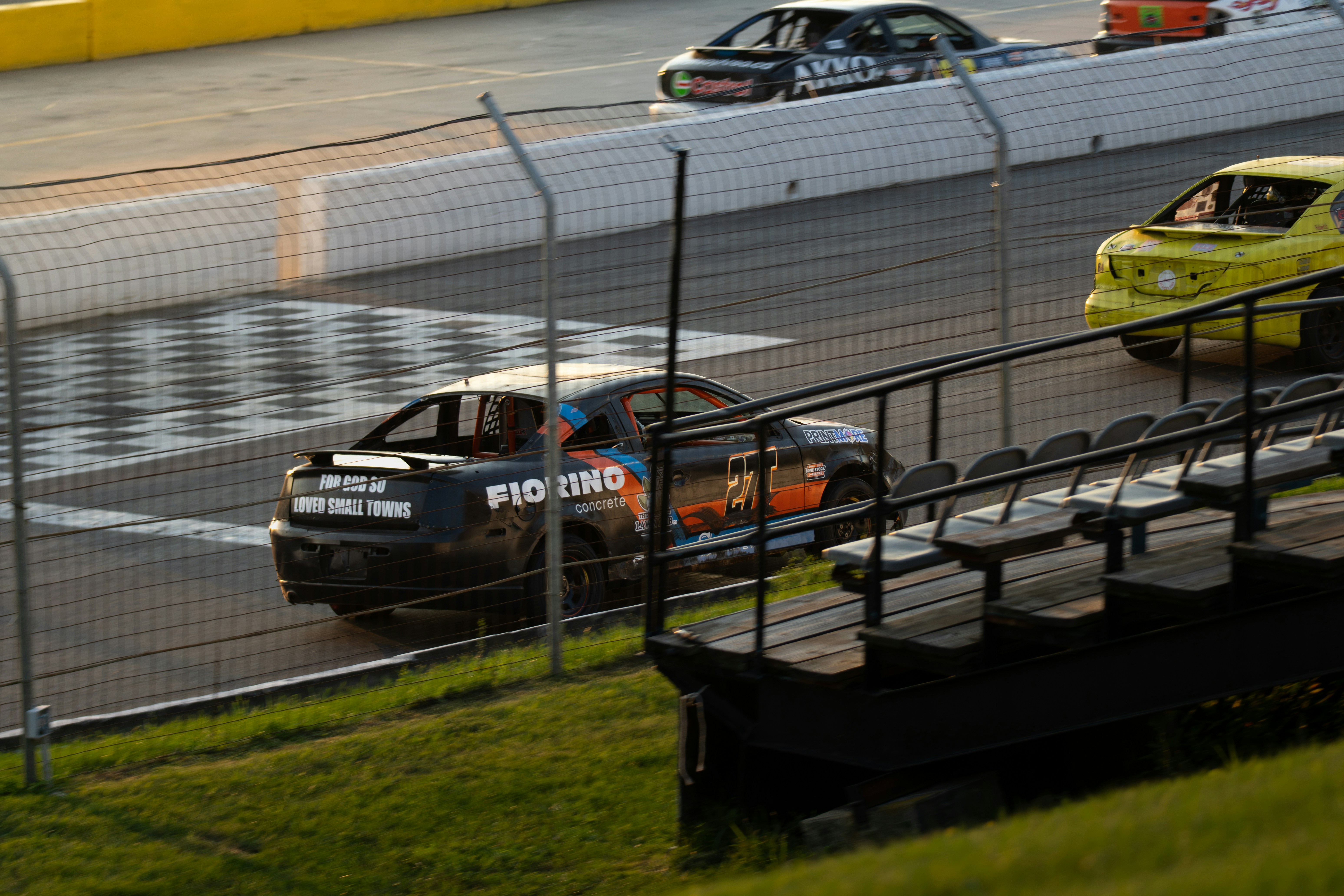 A black race car driving on a track past a yellow car