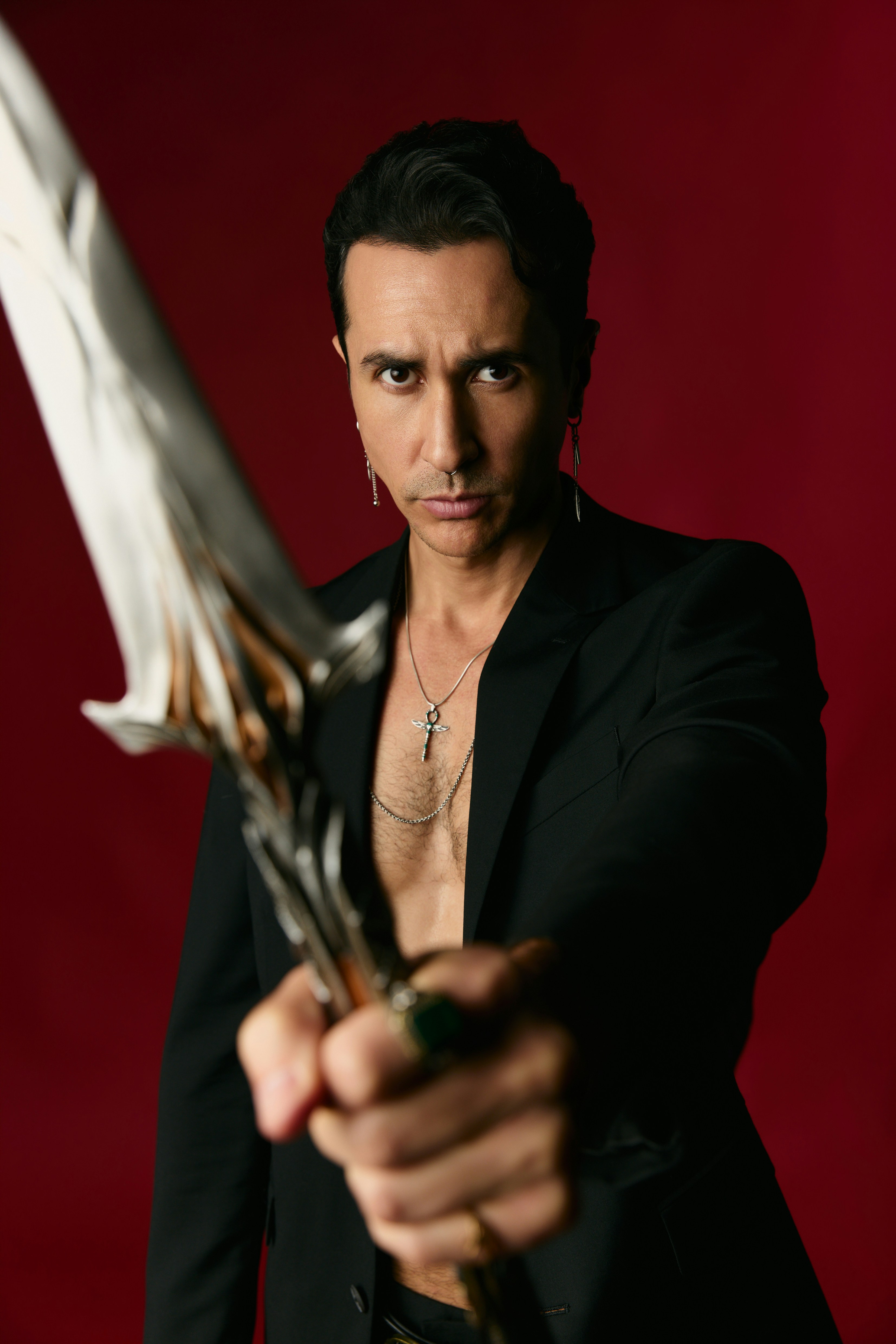 A man in a black blazer holding a decorative sword against a red background