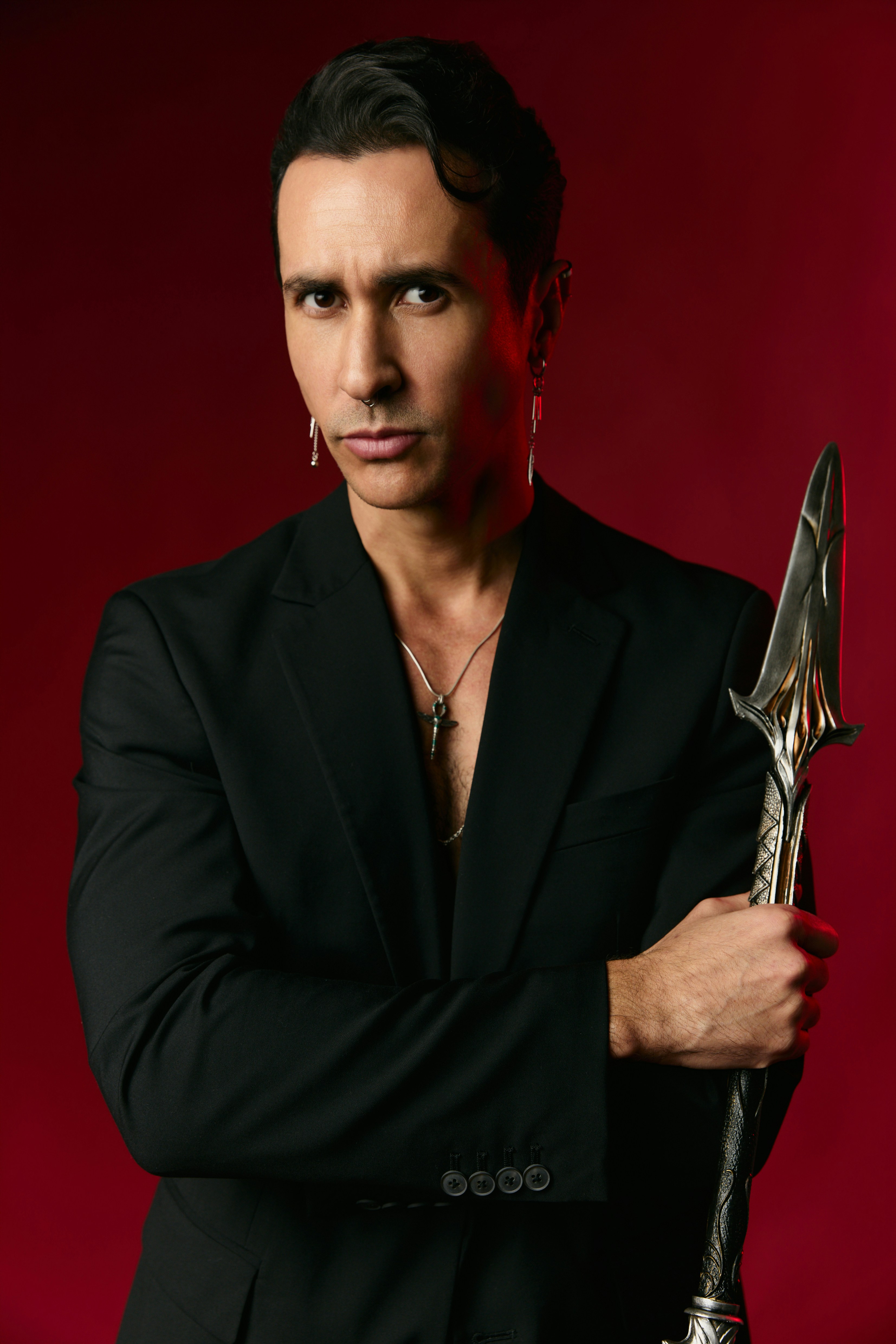A man in a black blazer holding a decorative spear against a red background