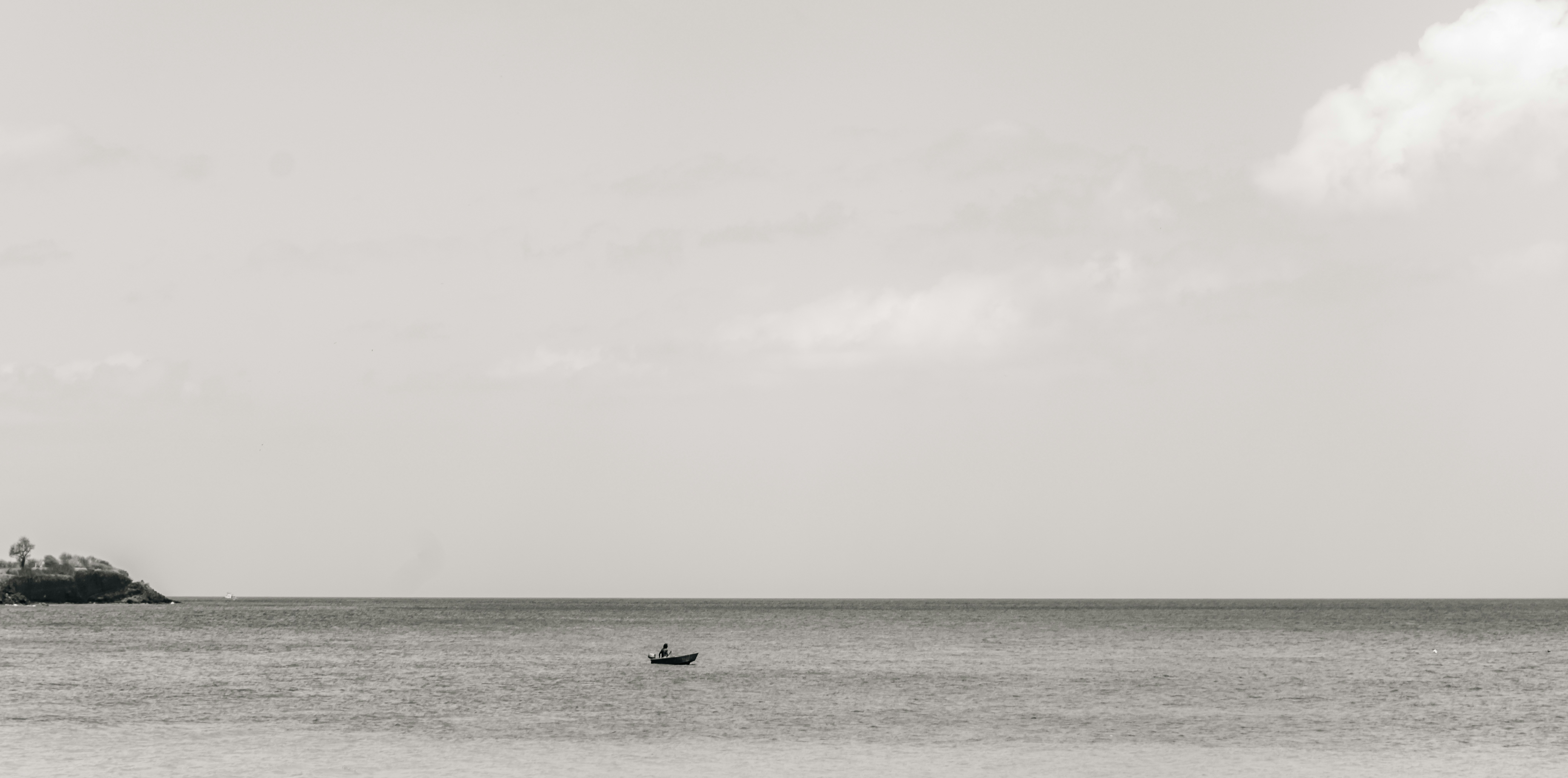 A small boat with a person on calm water under a cloudy sky