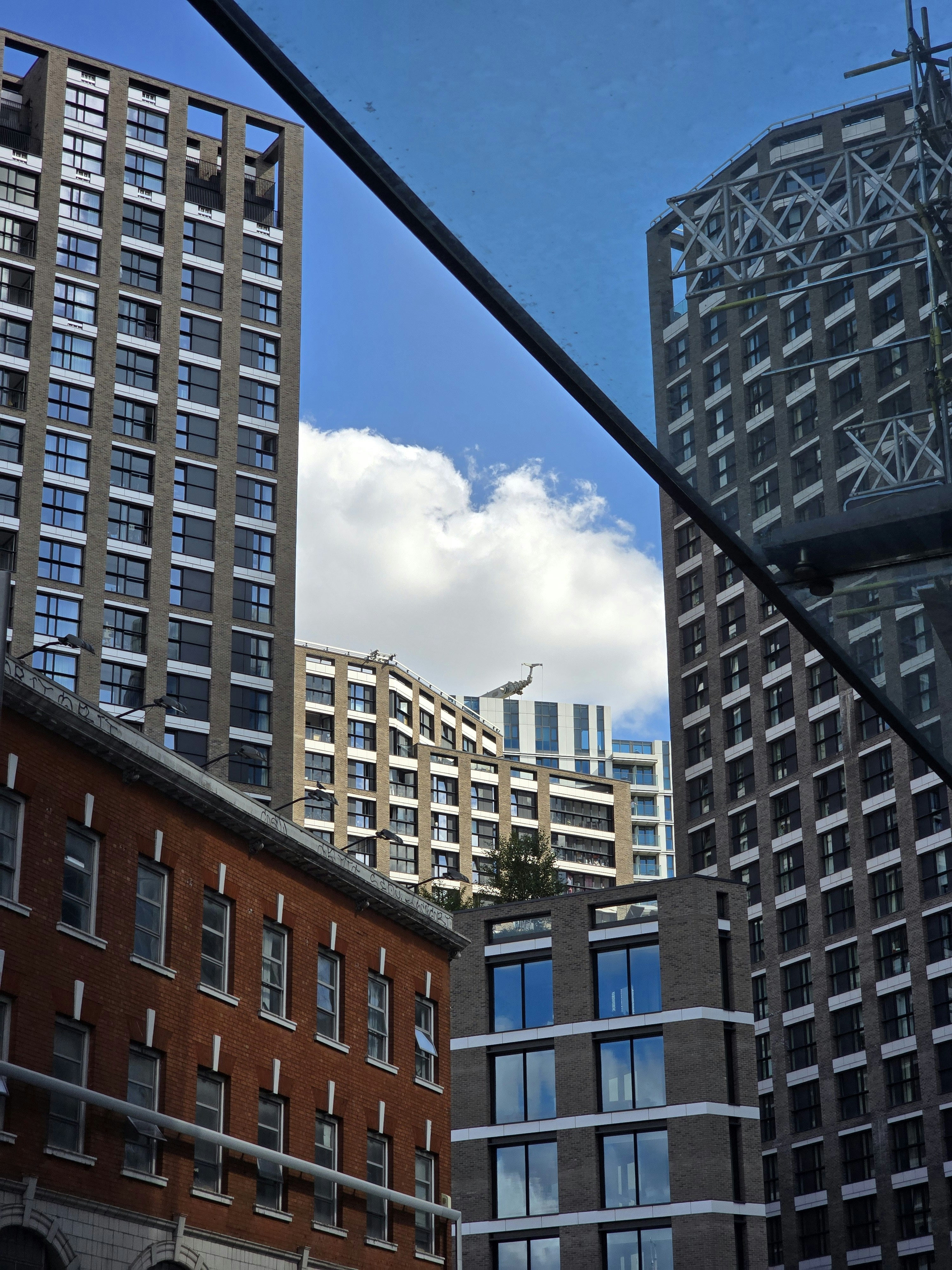 Modern high-rise apartment buildings surrounding a lower brick building under a blue sky