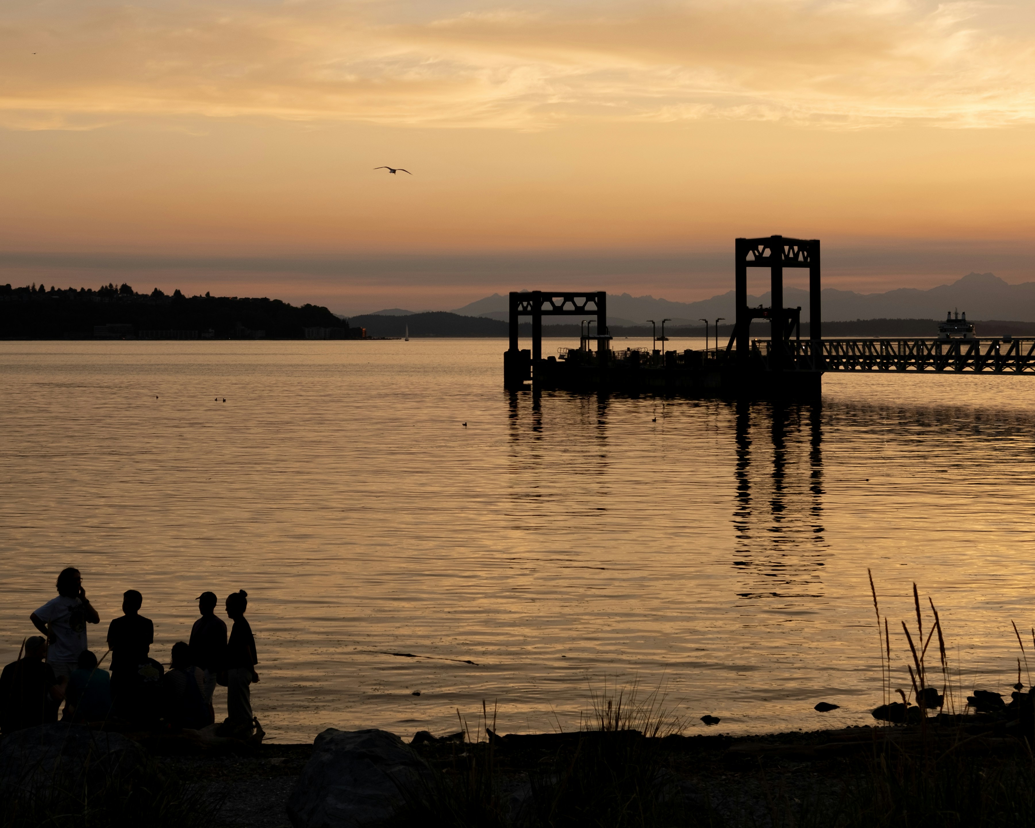Silhouettes de personnes sur une plage au soleil bas près d’un terminal de ferry