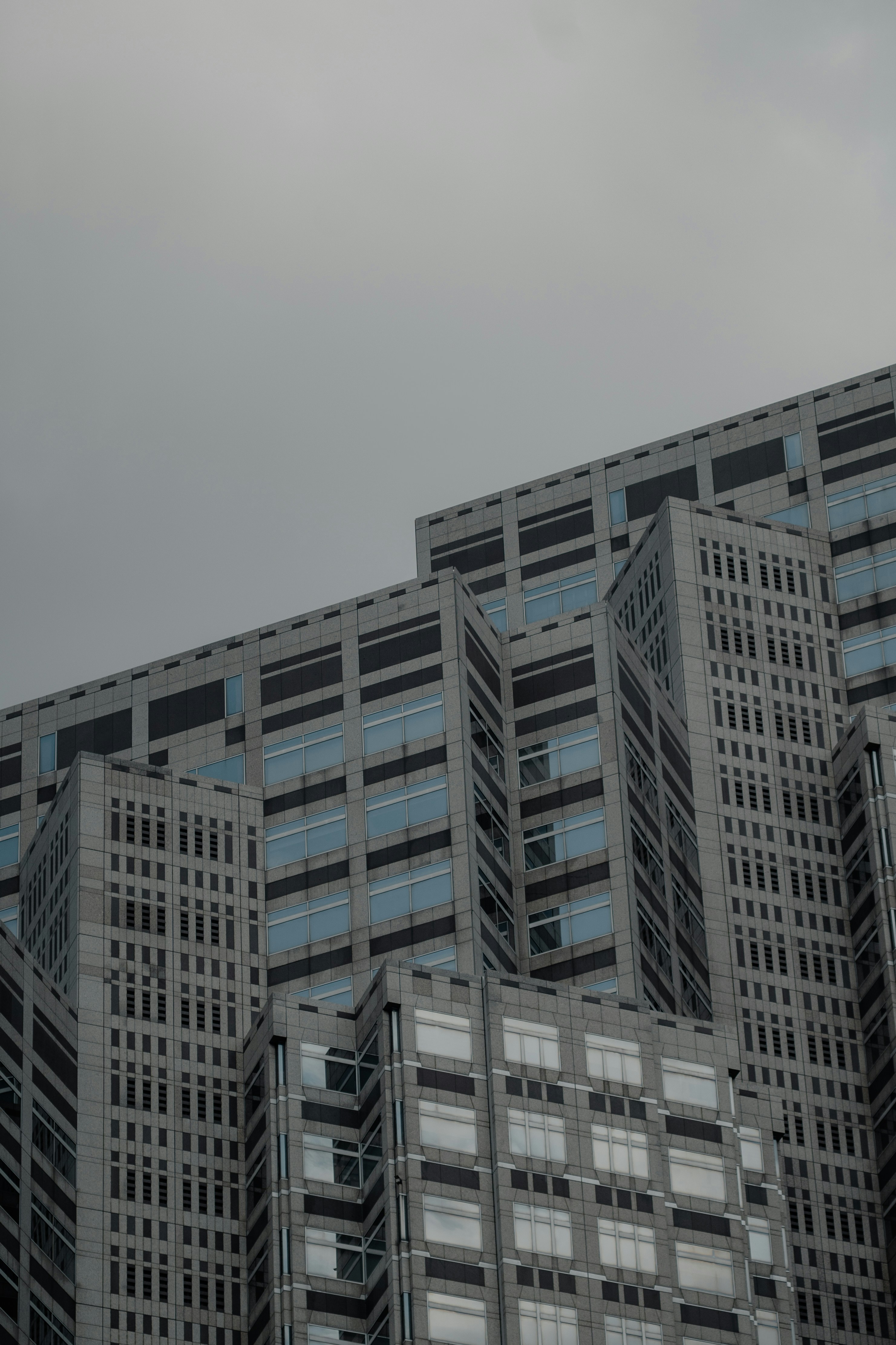A modern skyscraper with grey stone panels and grid windows against a cloudy sky