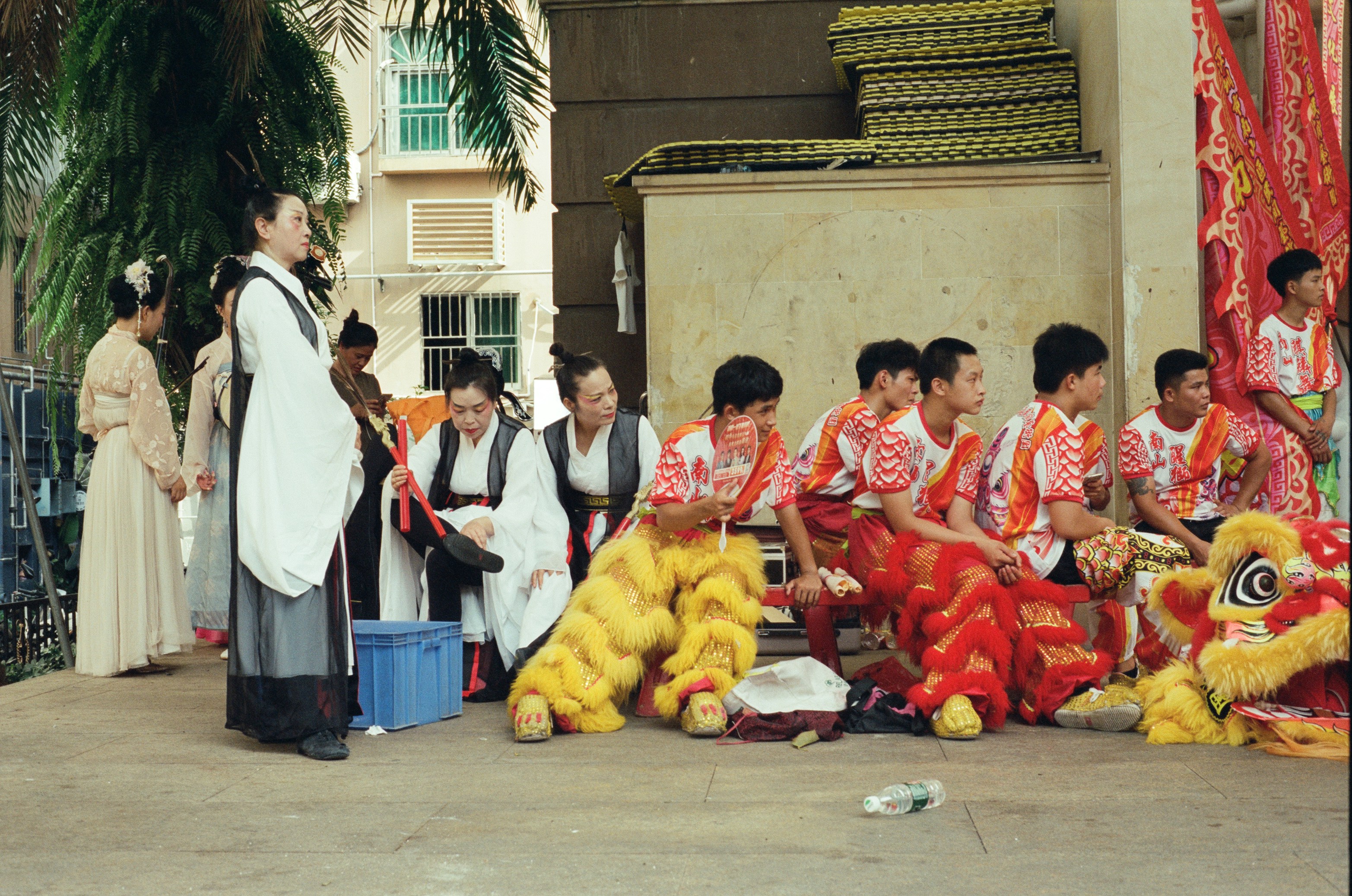 Performers in traditional costumes and lion dance outfits resting on a city street