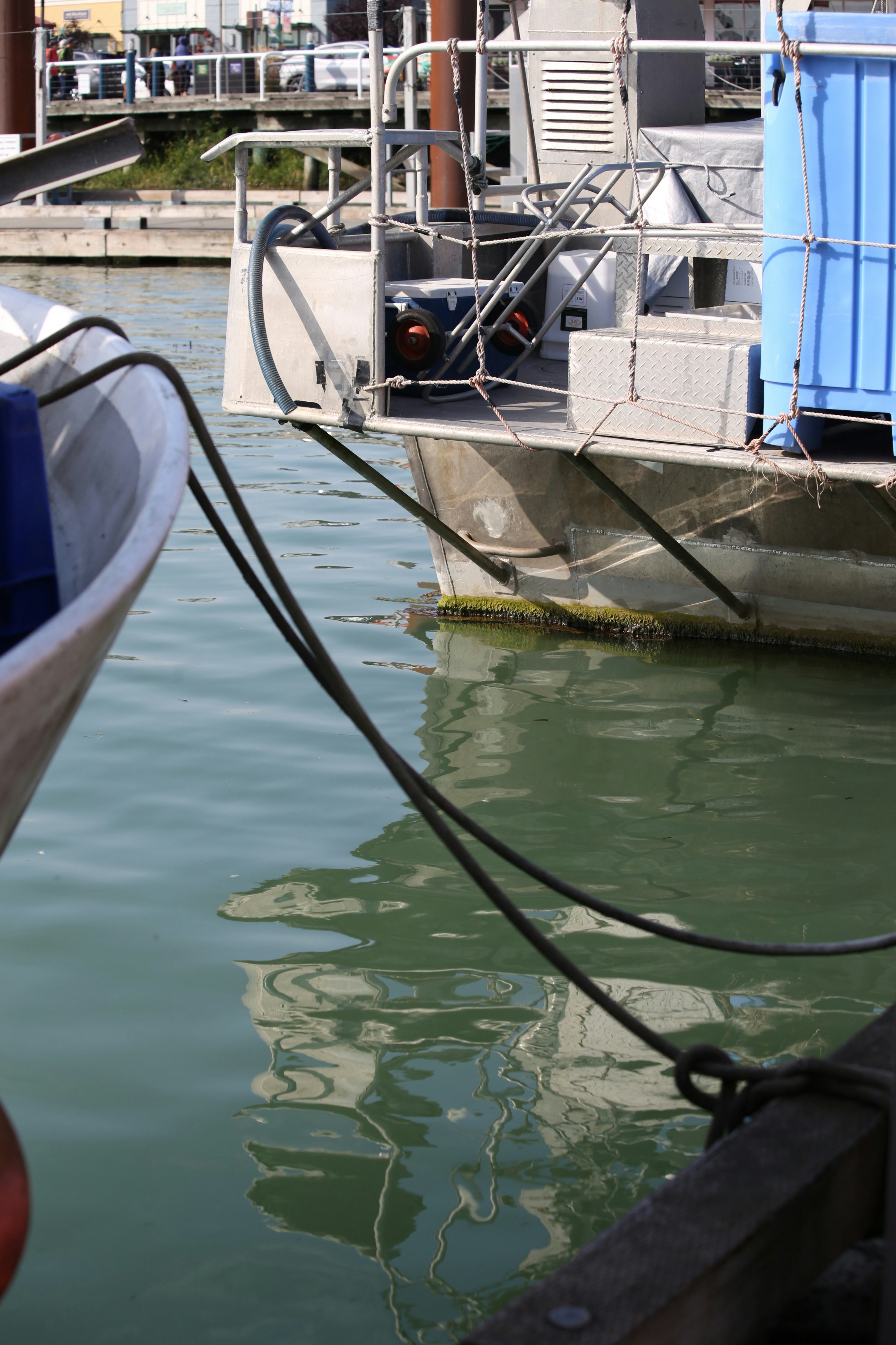 A metal fishing boat moored at a dock with a blue plastic crate