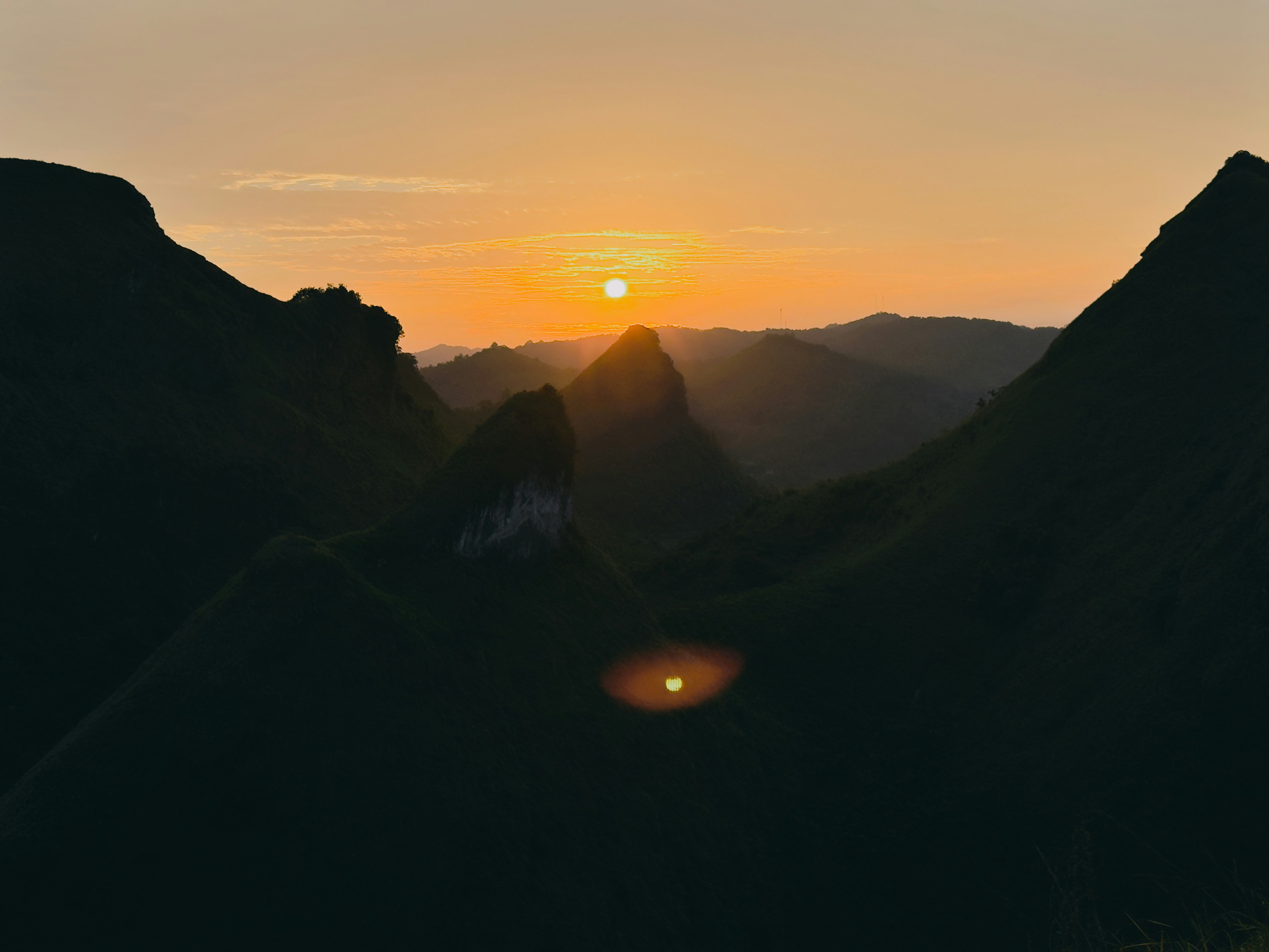 Low sun over dark mountain silhouettes against a warm orange sky