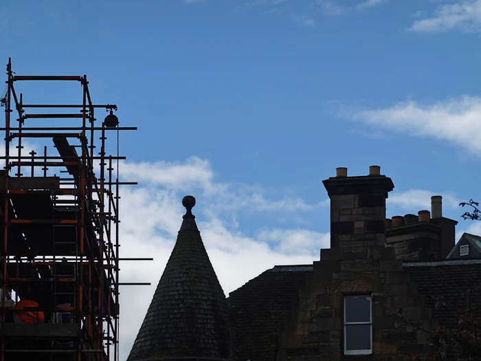 Scaffolding beside a stone building with a chimney