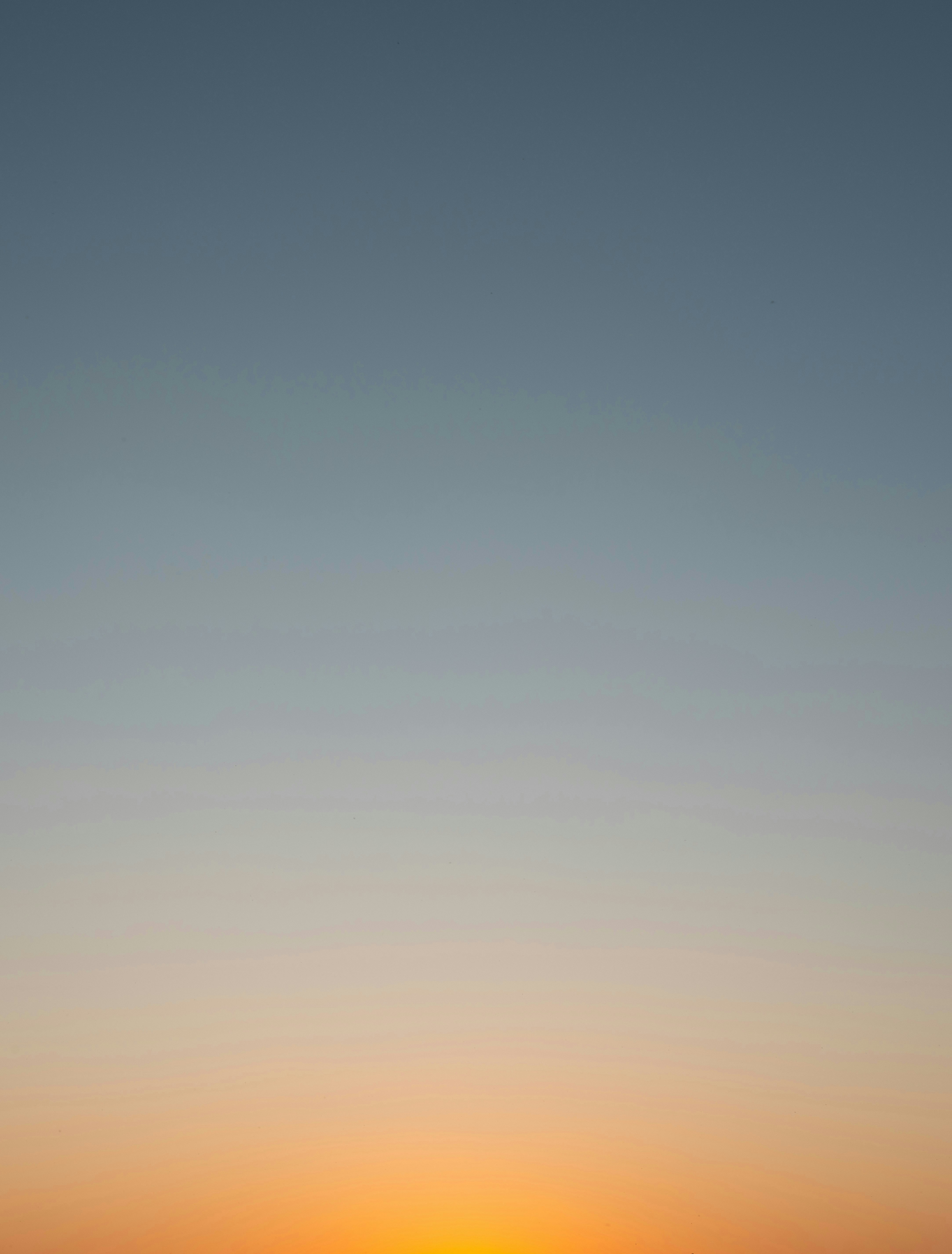 A smooth gradient shifting from a pale blue sky to a warm orange horizon
