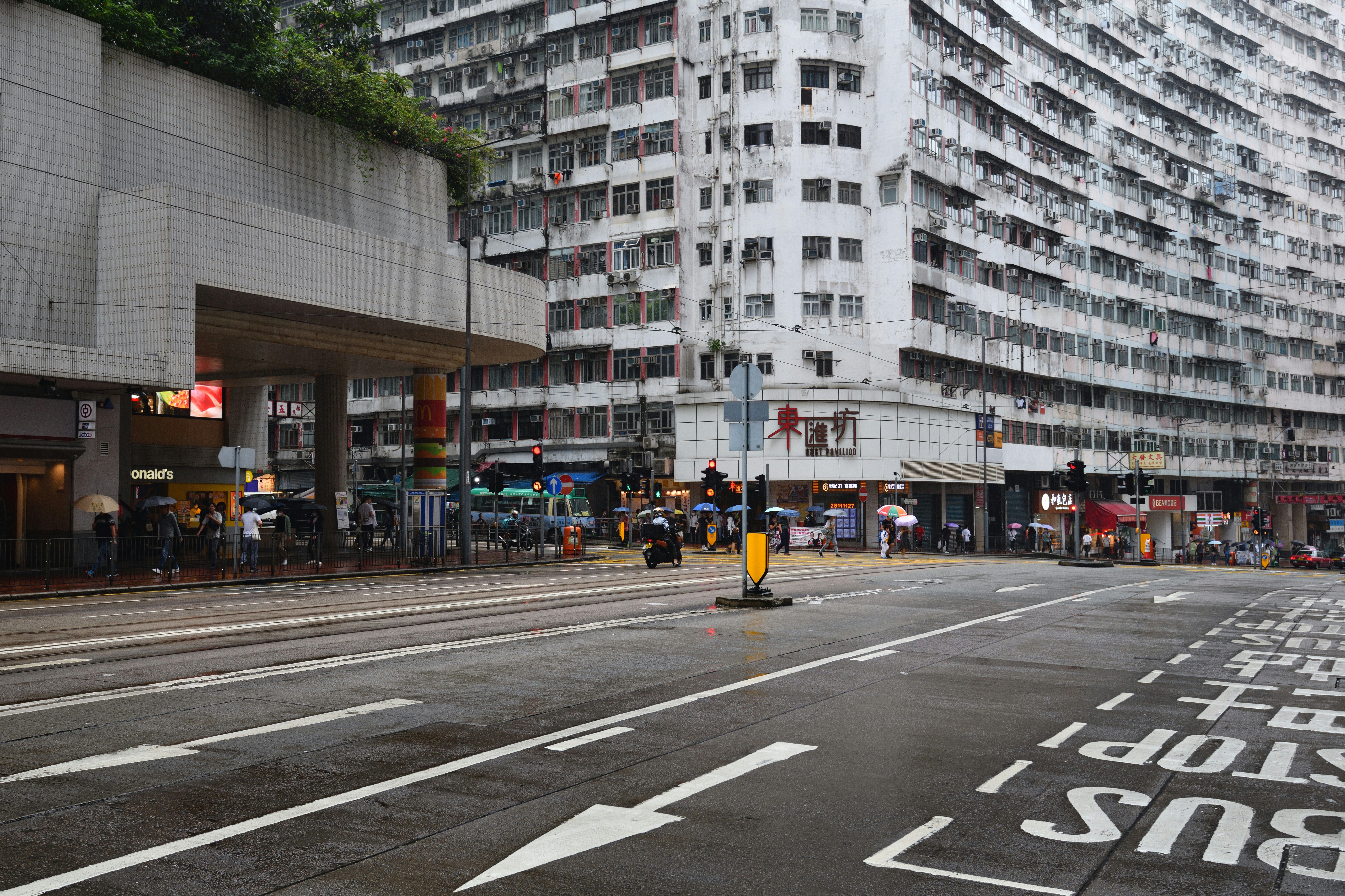 Wet city road with a painted bus lane and pedestrians with umbrellas