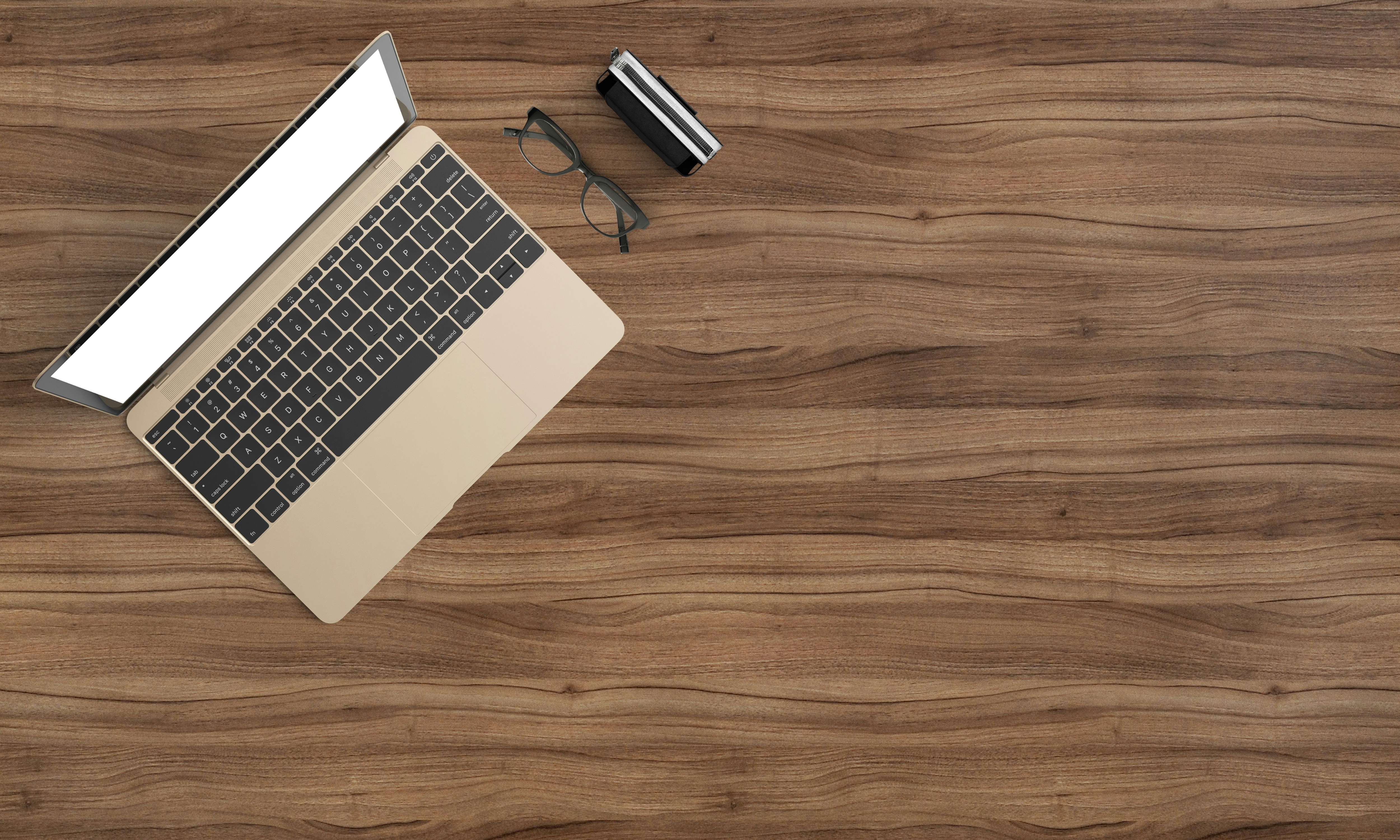 A laptop with a blank screen, glasses, and a small case on a wooden desk