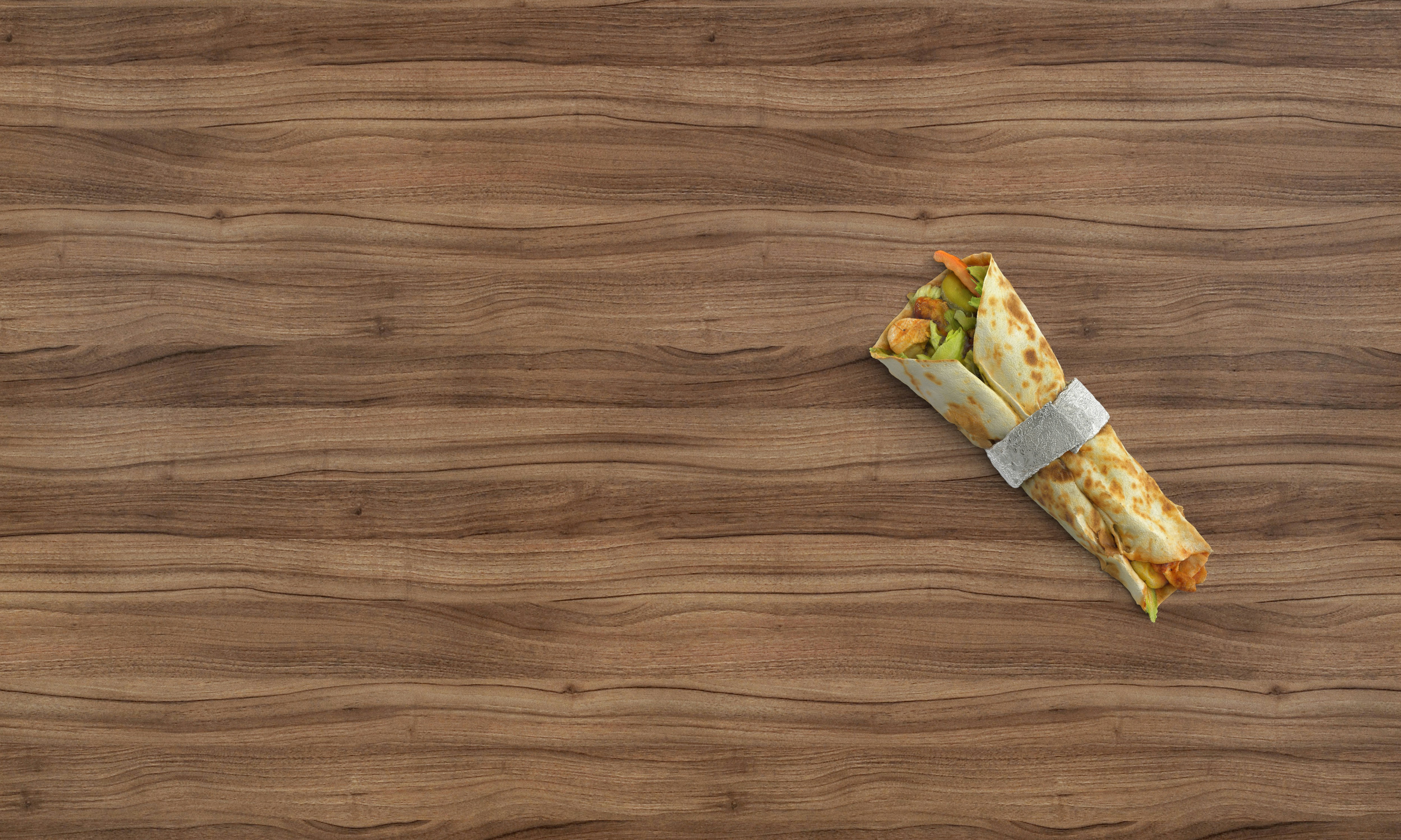 A chicken wrap with vegetables in a foil band on a wooden surface