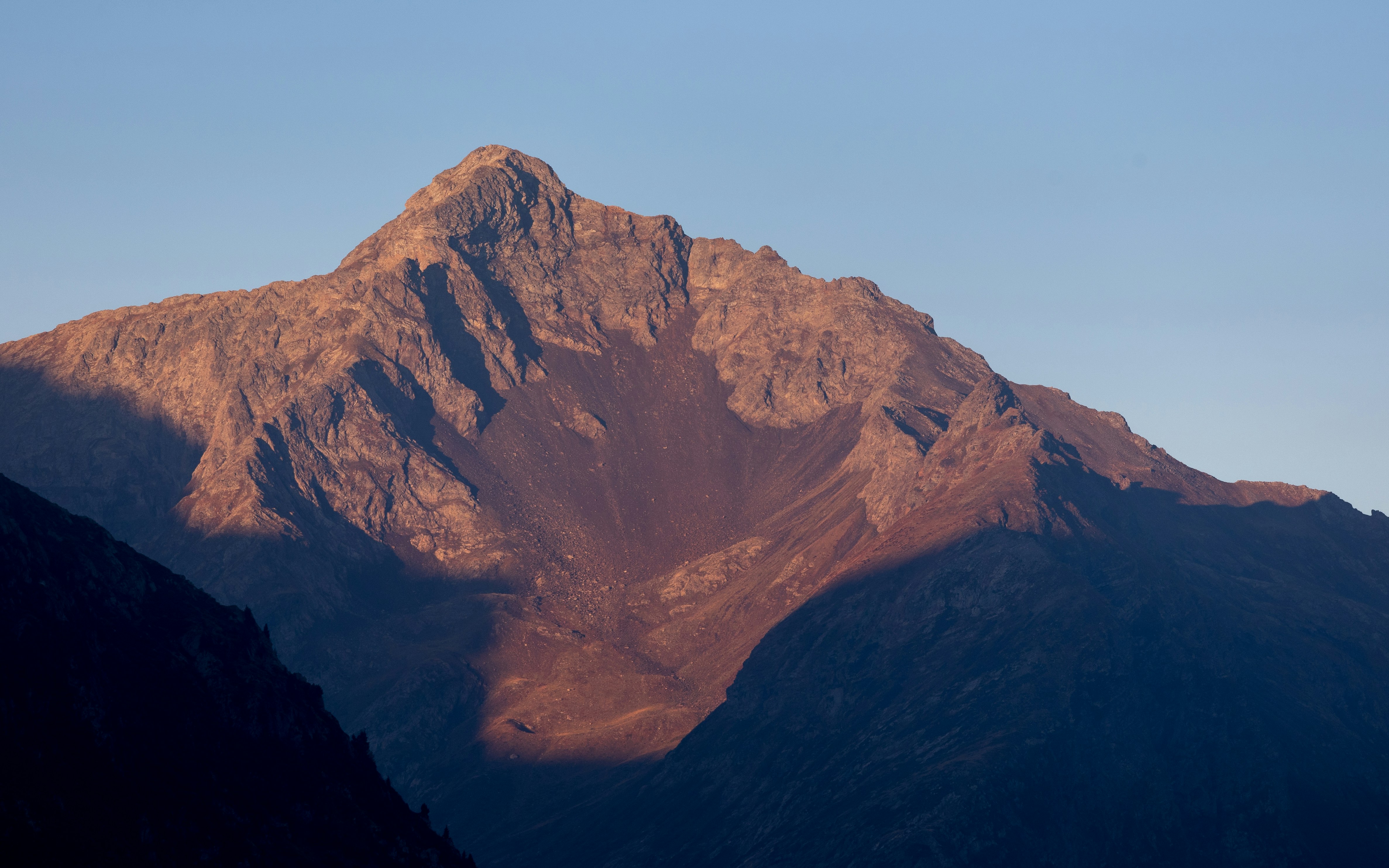 A rocky mountain peak illuminated by low golden light against a clear blue sky
