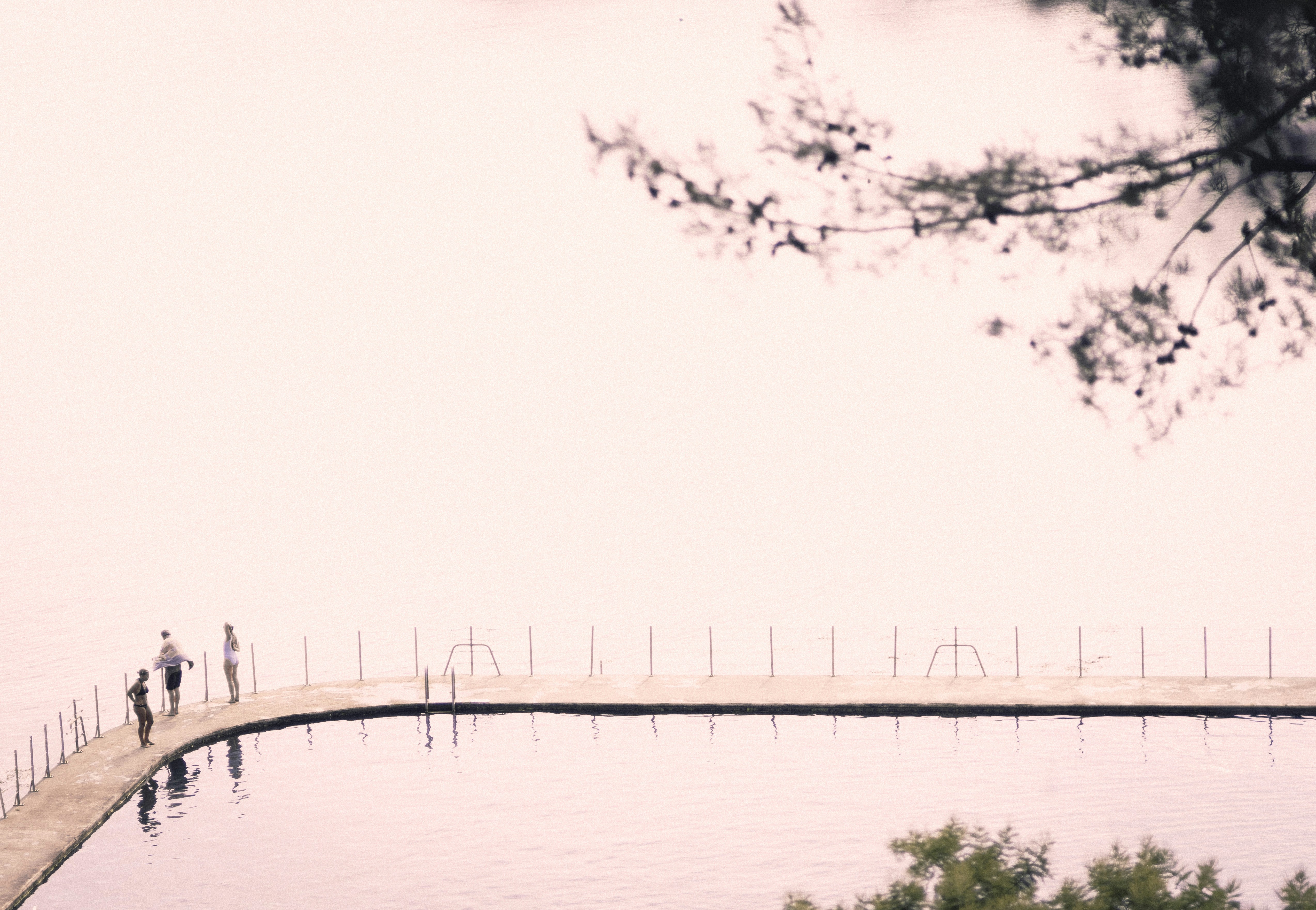 Three people on a curved concrete pool edge beside a calm body of water
