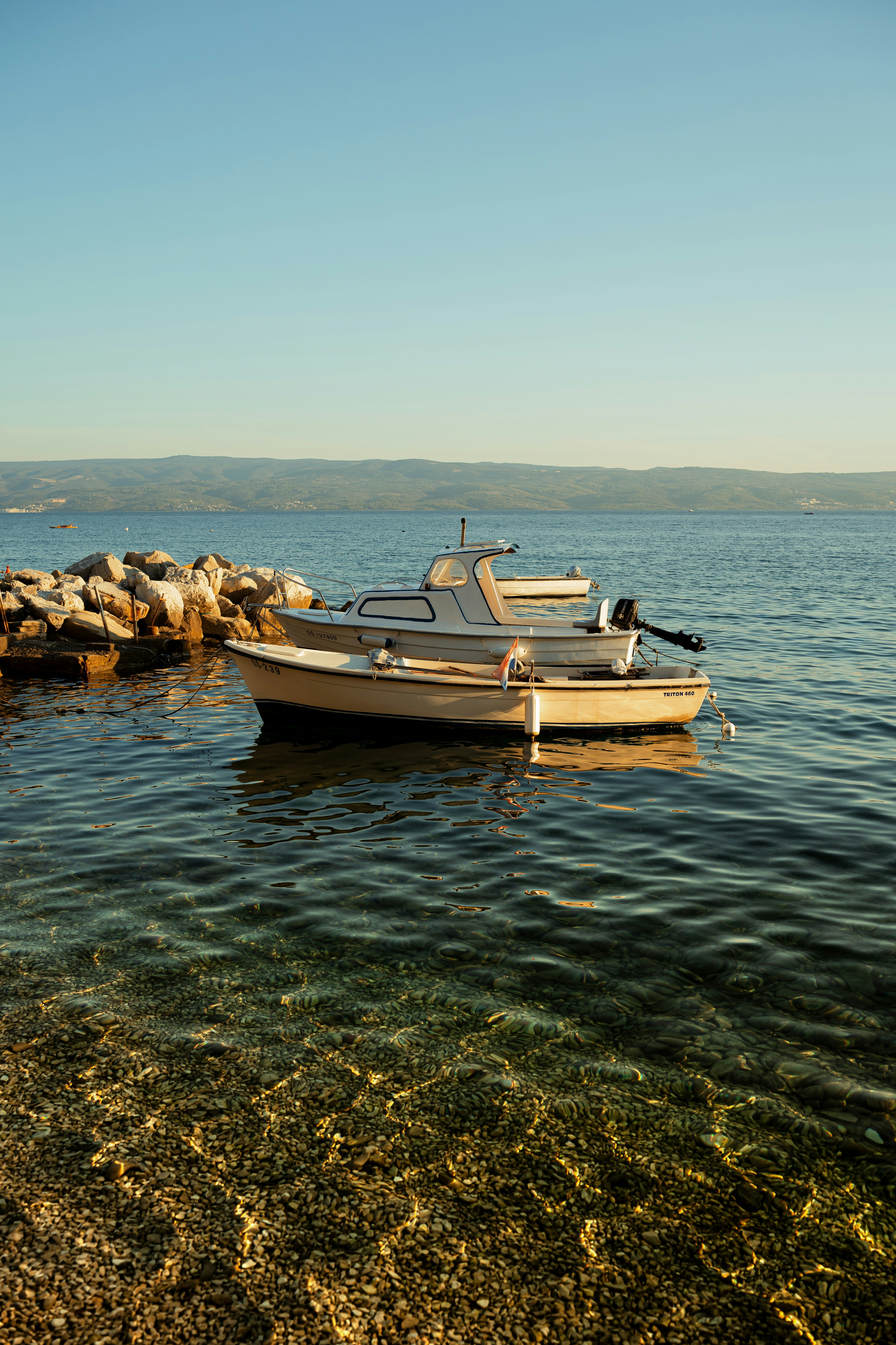 Two small motorboats moored in clear water near a rocky breakwater at low sun