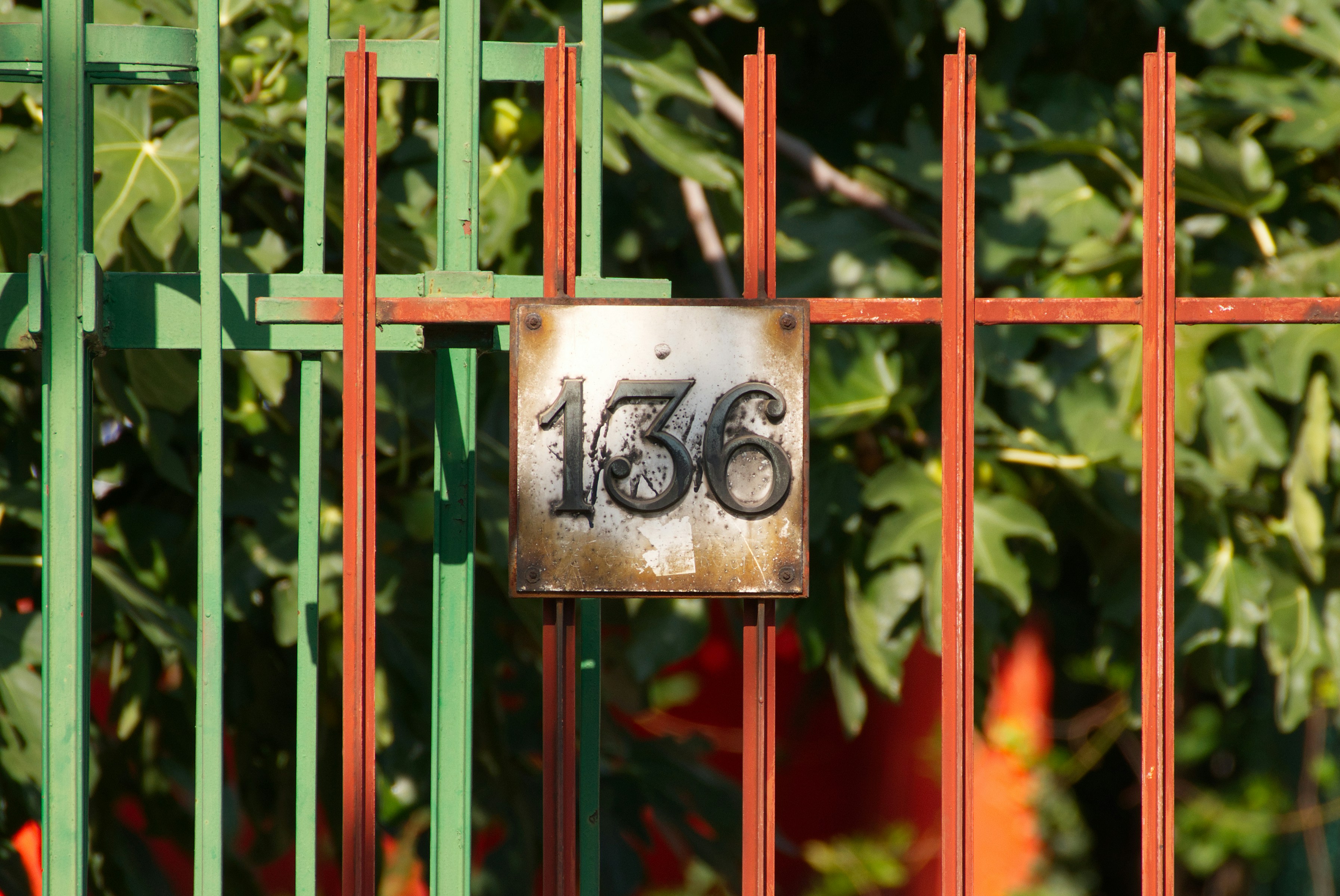 A metal sign with the number 136 on a green and red fence