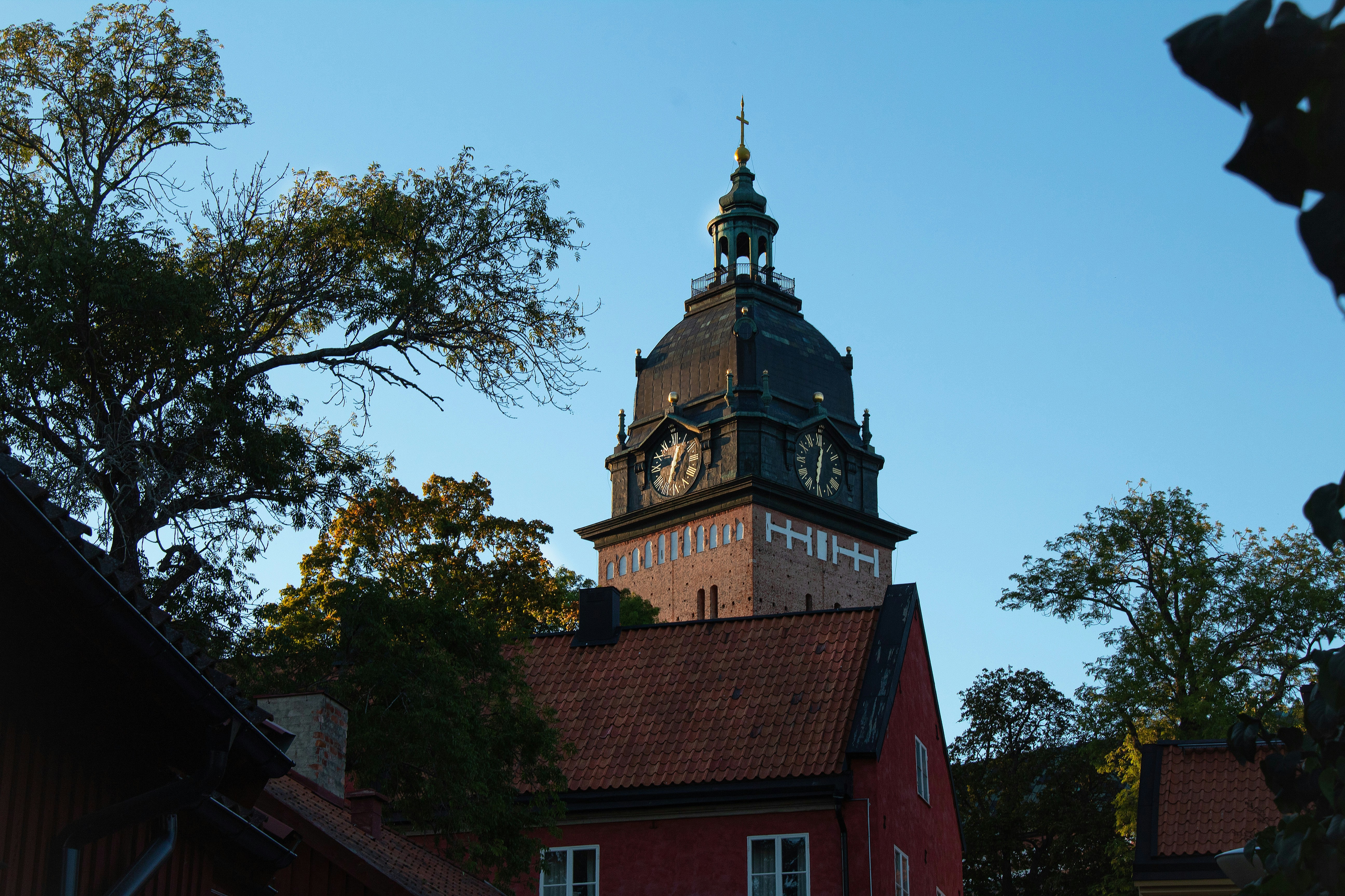A tall brick clock tower rising above red roofed buildings against a blue sky