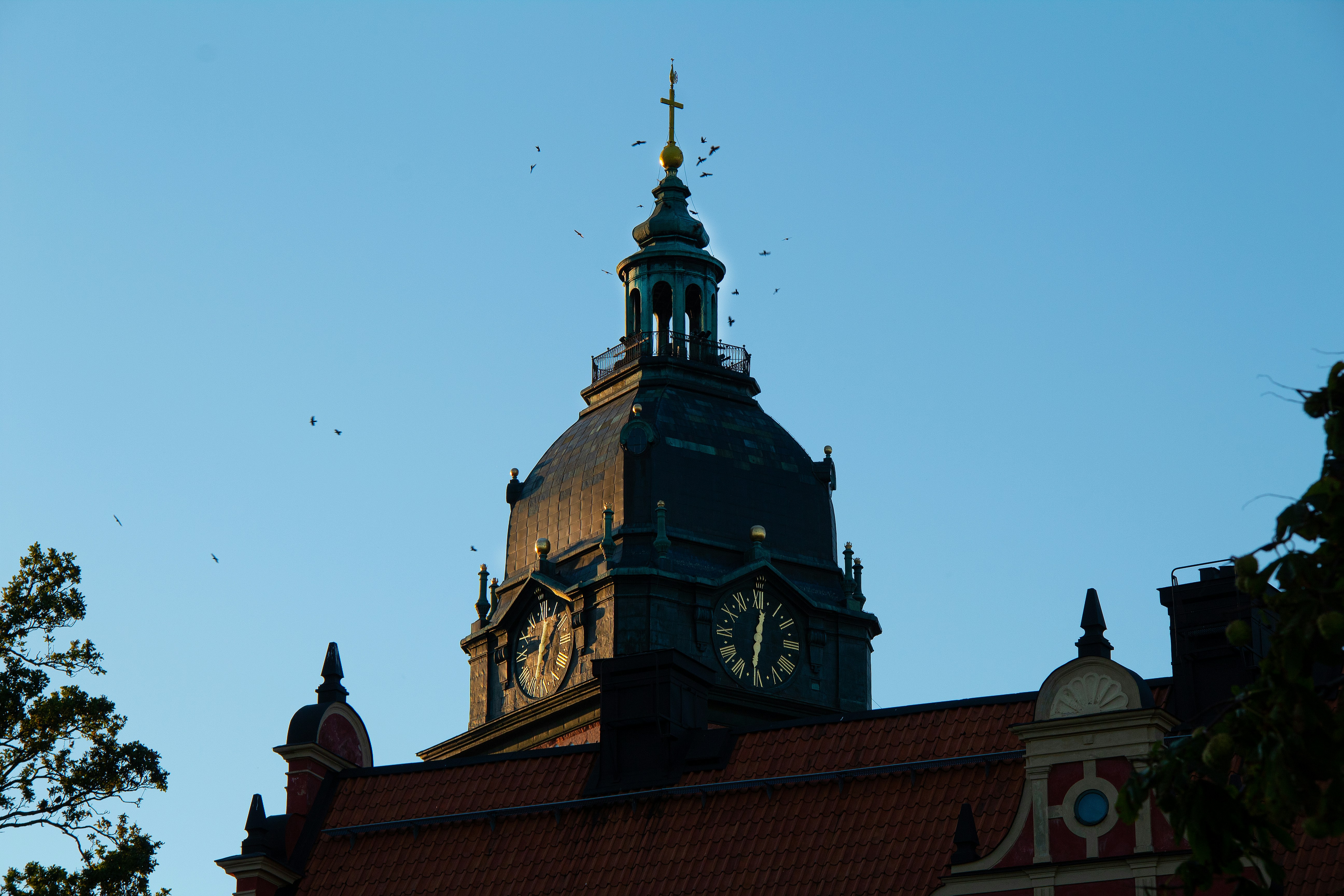 A dark clock tower with a copper dome against a clear blue sky