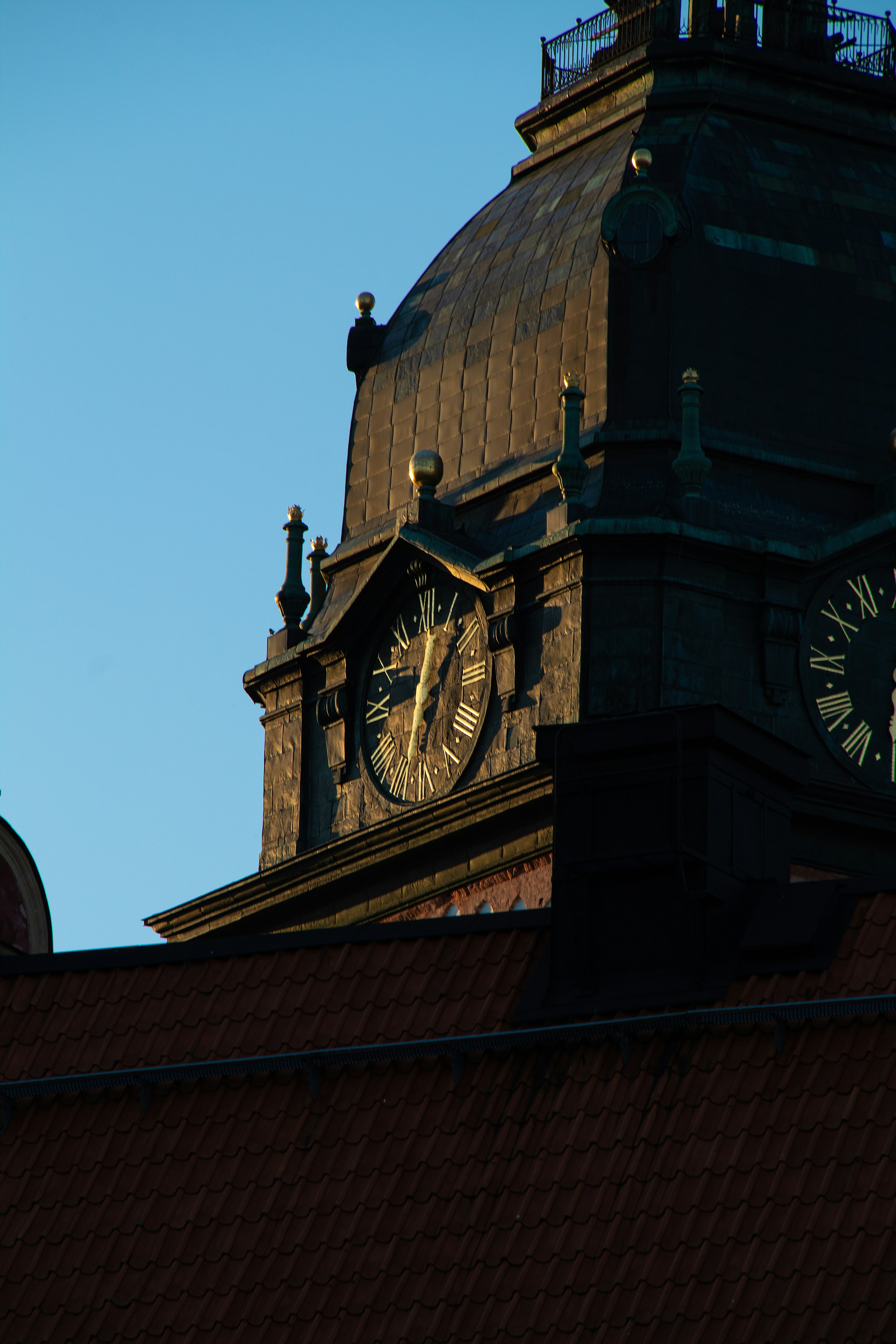 A dark clock tower with Roman numerals against a clear blue sky