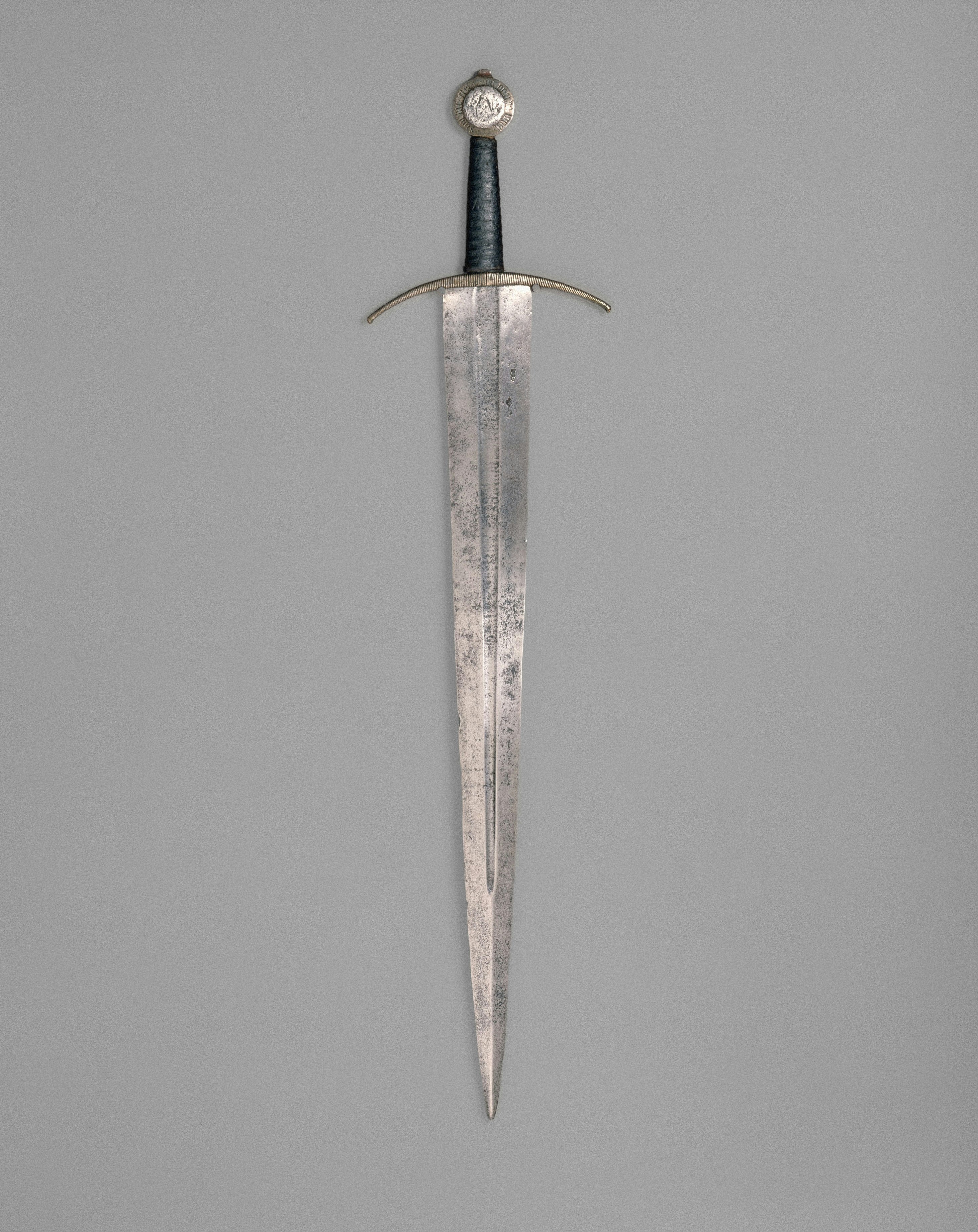 A medieval sword with a dark grip and a circular pommel on grey