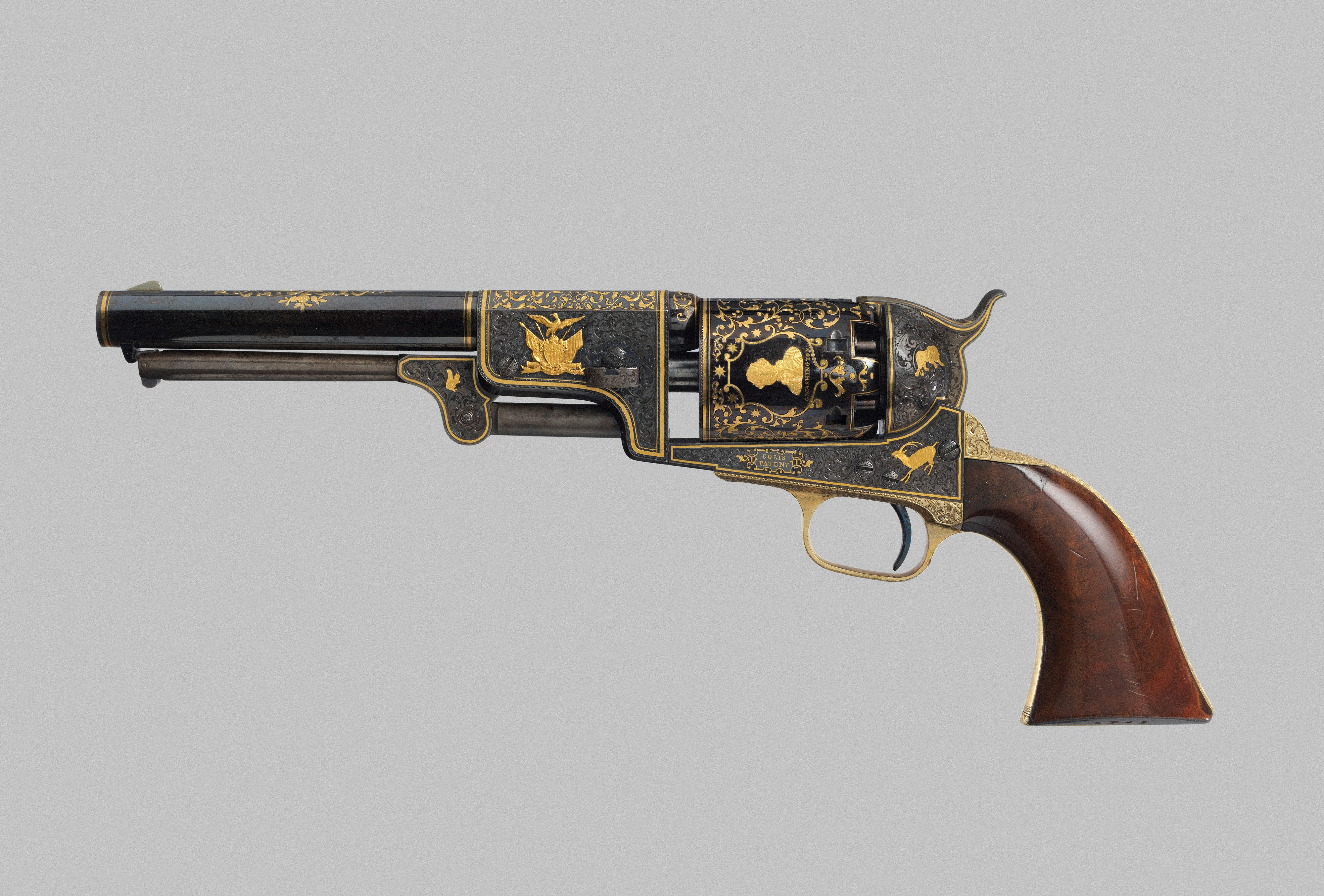 An ornate antique revolver with gold inlay and a wooden grip on grey