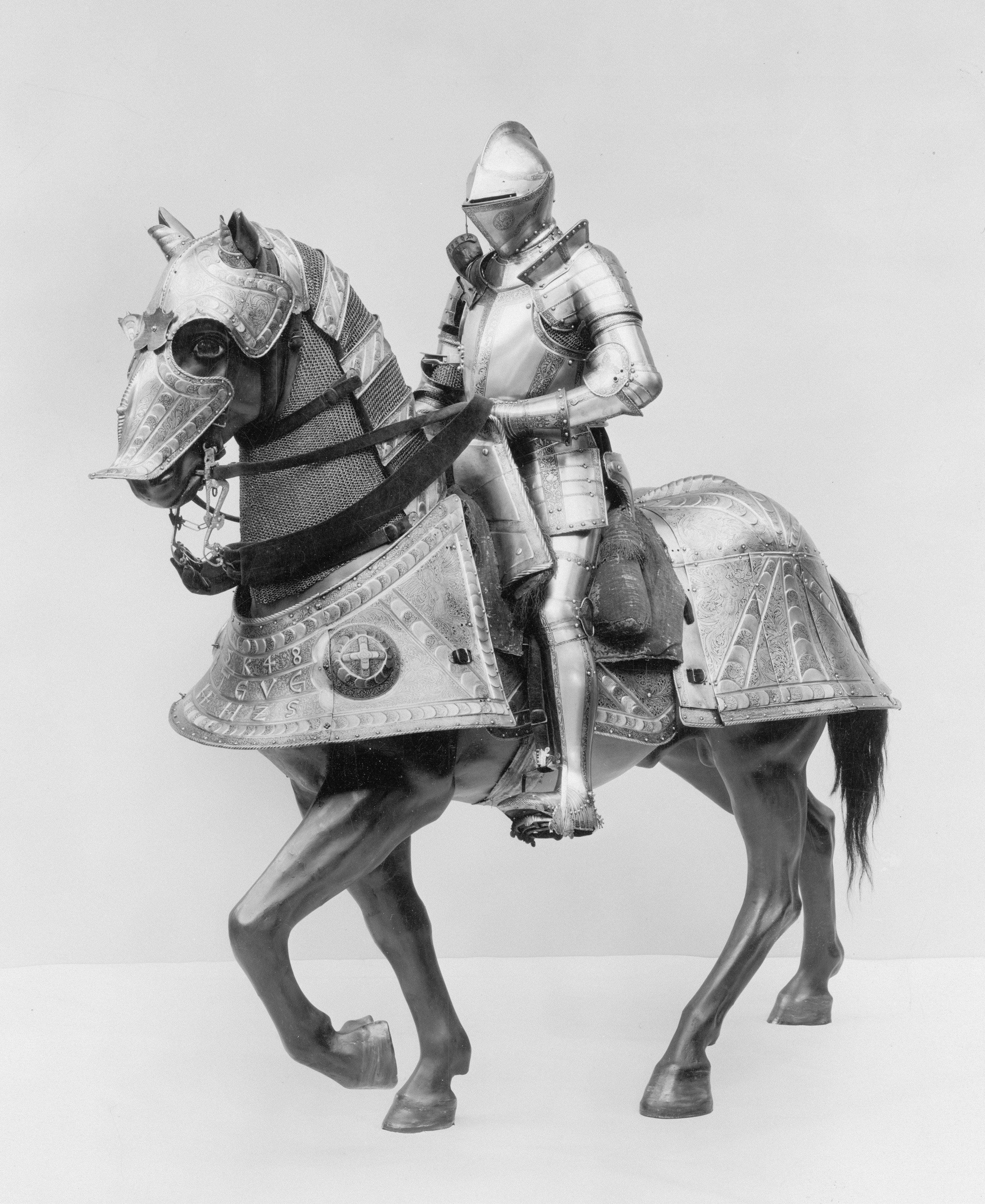 A knight in polished steel armor riding a horse with ornate metal barding