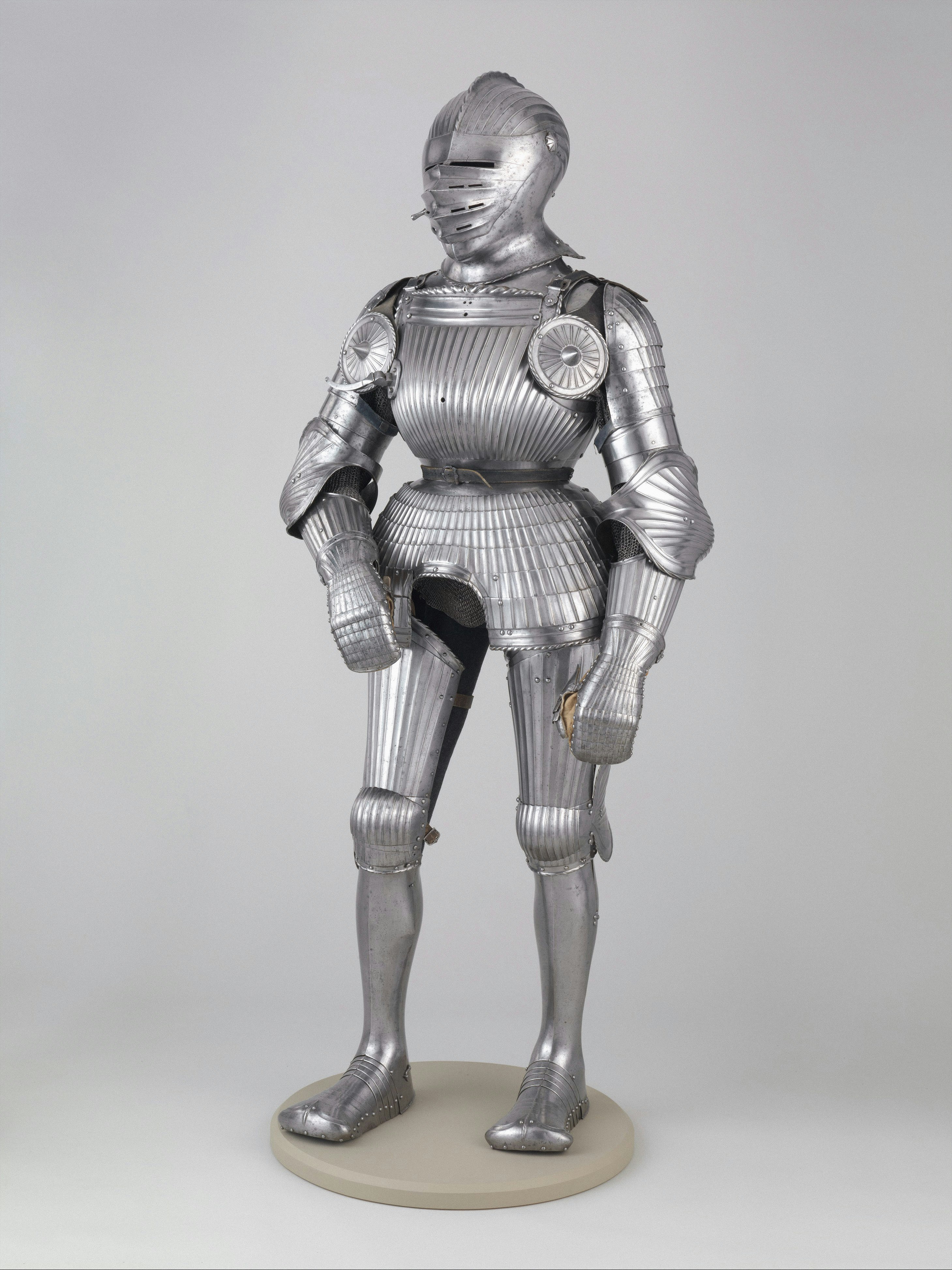 A suit of polished steel plate armor with fluted details on a stand